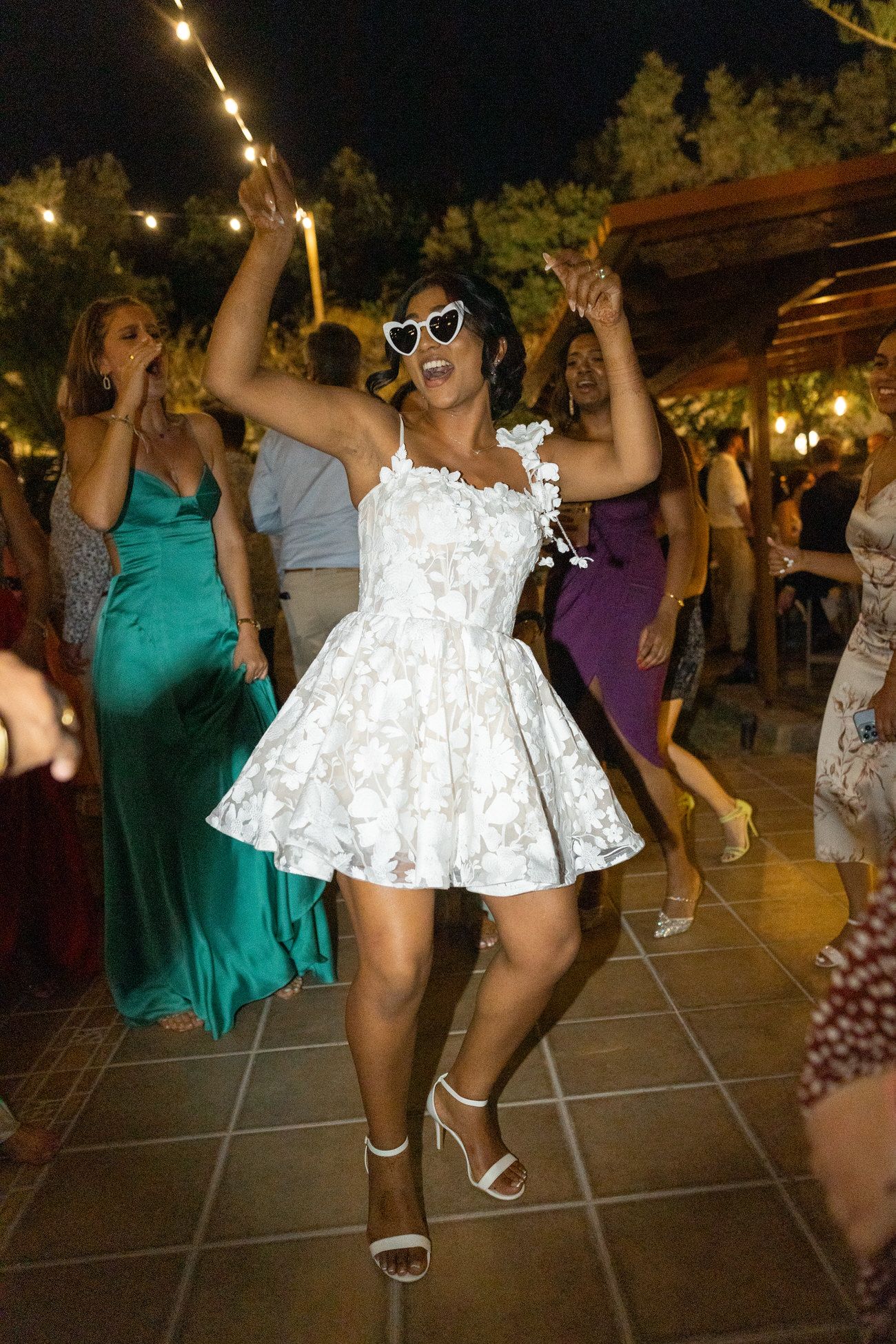 Guests dancing at a wedding reception with festive string lights overhead.