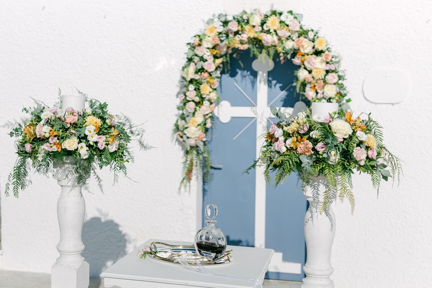 A white archway decorated with yellow and cream floral arrangements and greenery against a white wall.