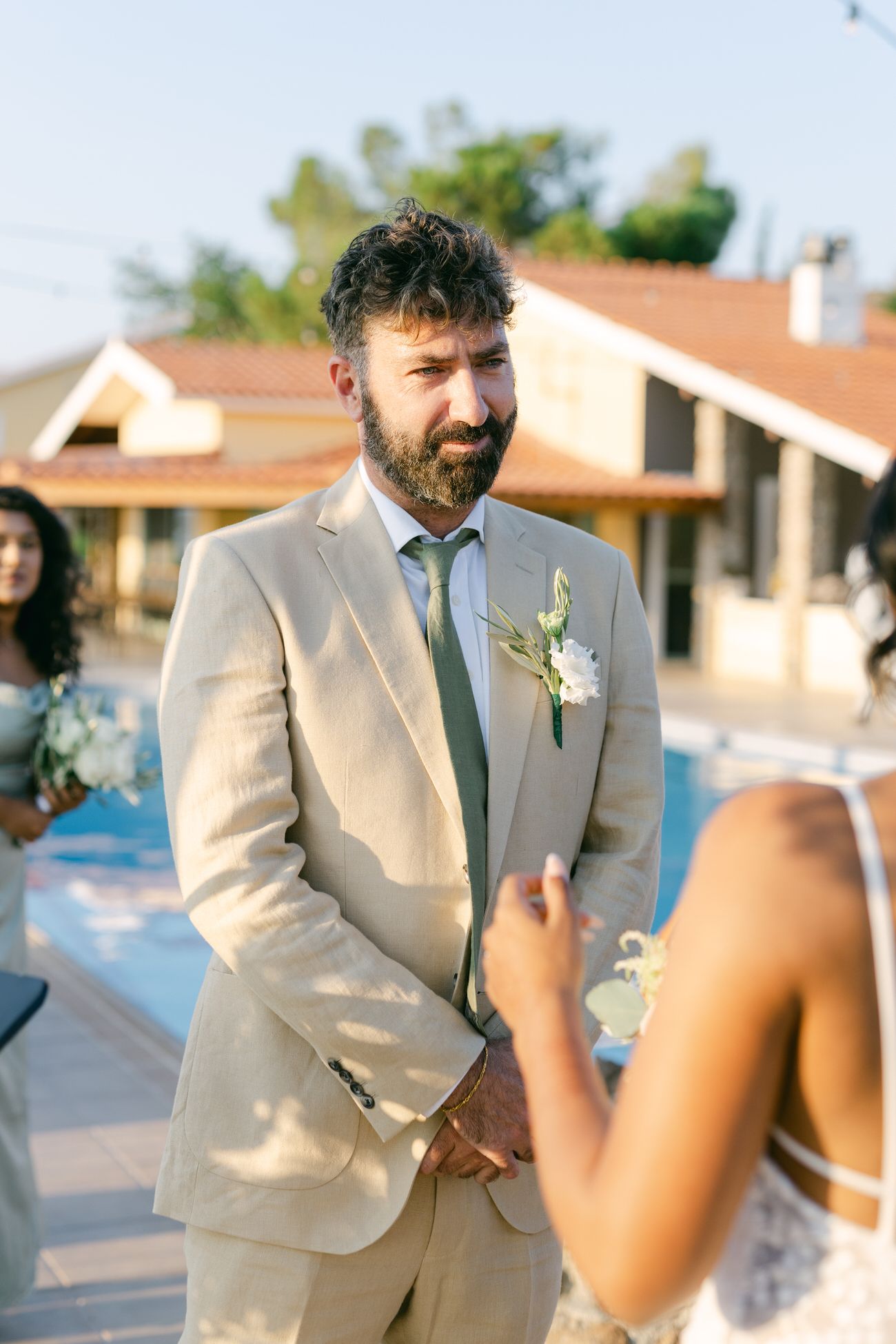 Groom in beige suit waiting during outdoor wedding ceremony.