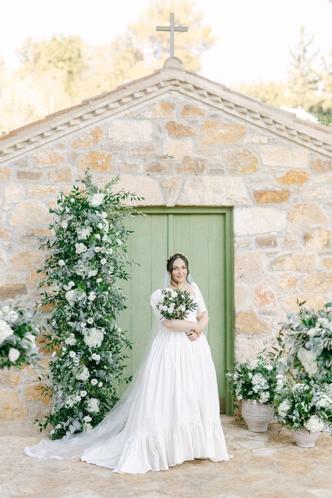 A rustic stone chapel with a green door features beautiful white floral arrangements and greenery for a romantic wedding setting.