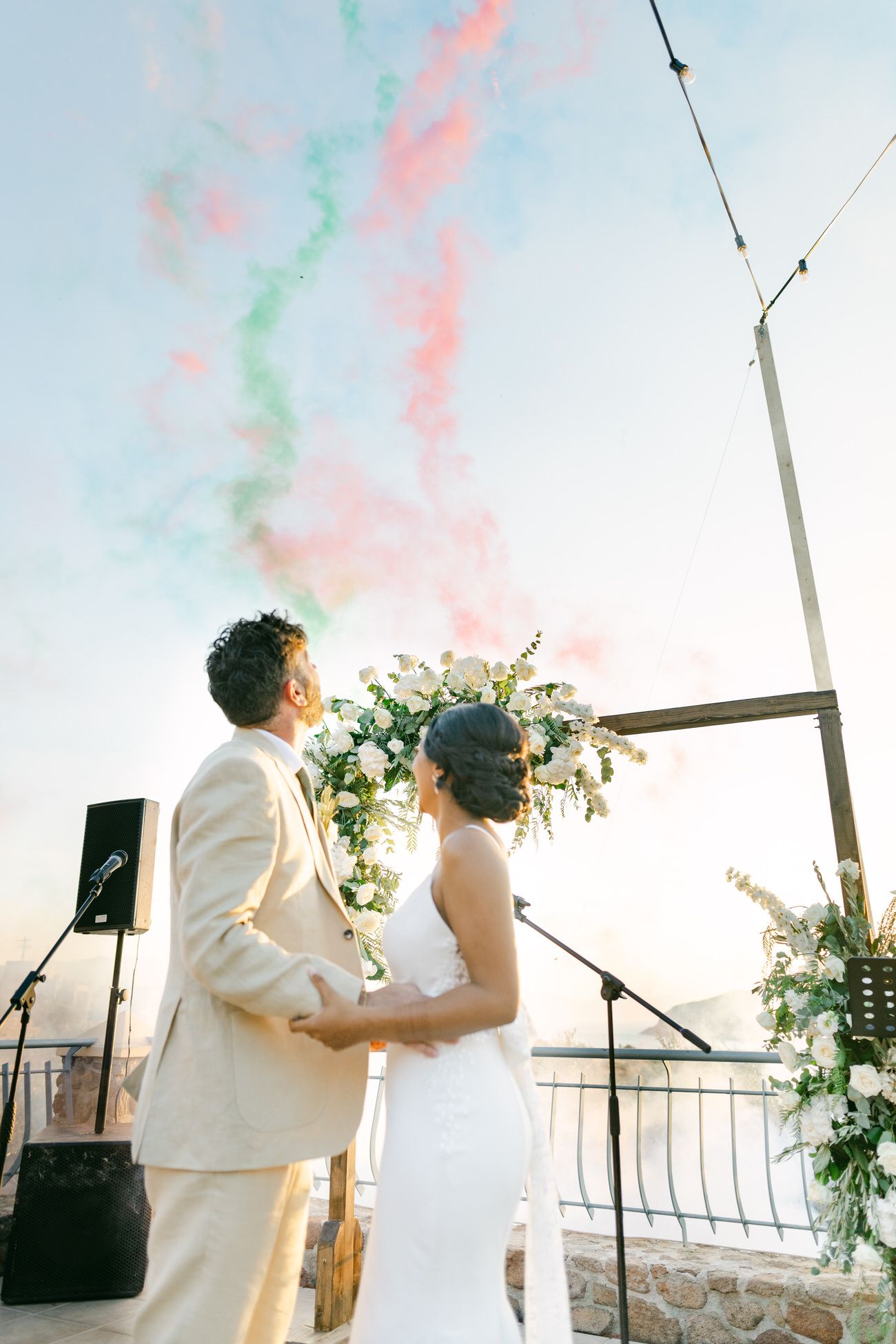 Couple holding hands under colorful smoke effects during sunset wedding celebration.