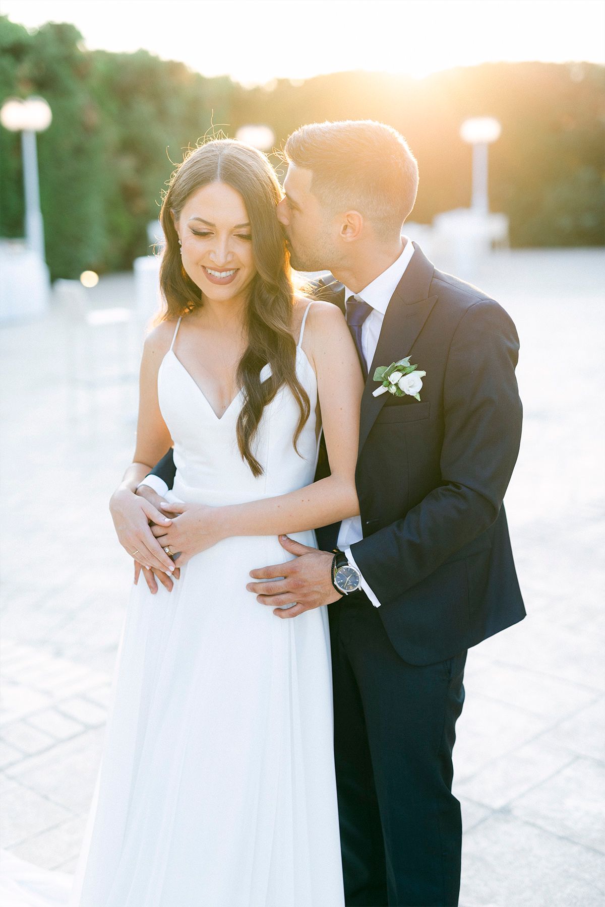 Newlyweds share an intimate moment at sunset while posing for wedding photos outdoors.