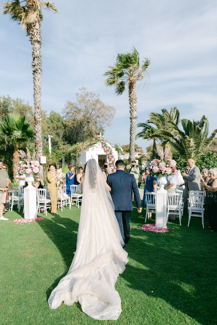 Outdoor wedding ceremony setup with palm trees and white chairs on manicured lawn.