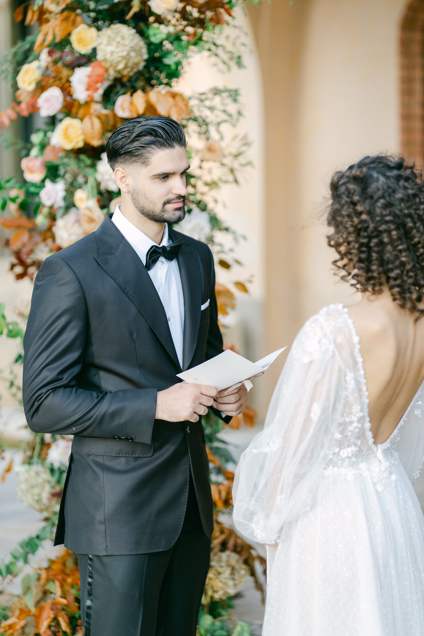 Couple exchanges vows during outdoor wedding ceremony with beautiful floral arrangements of peach and cream blooms.