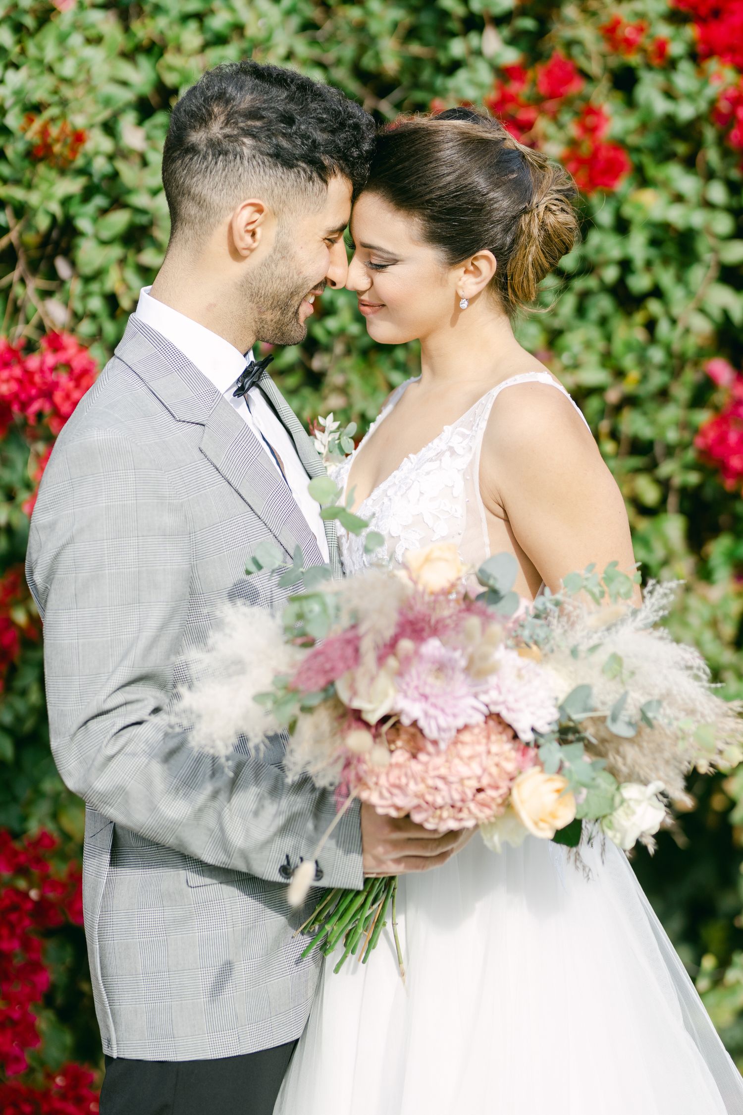 A romantic wedding portrait with a pastel bouquet against a backdrop of red flowers.