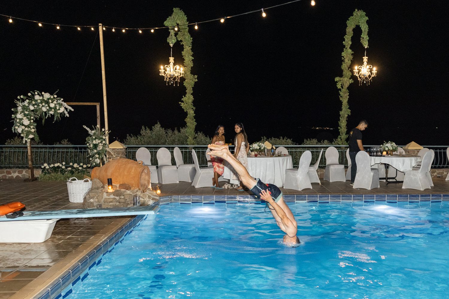 Someone diving into an illuminated pool during a nighttime celebration.
