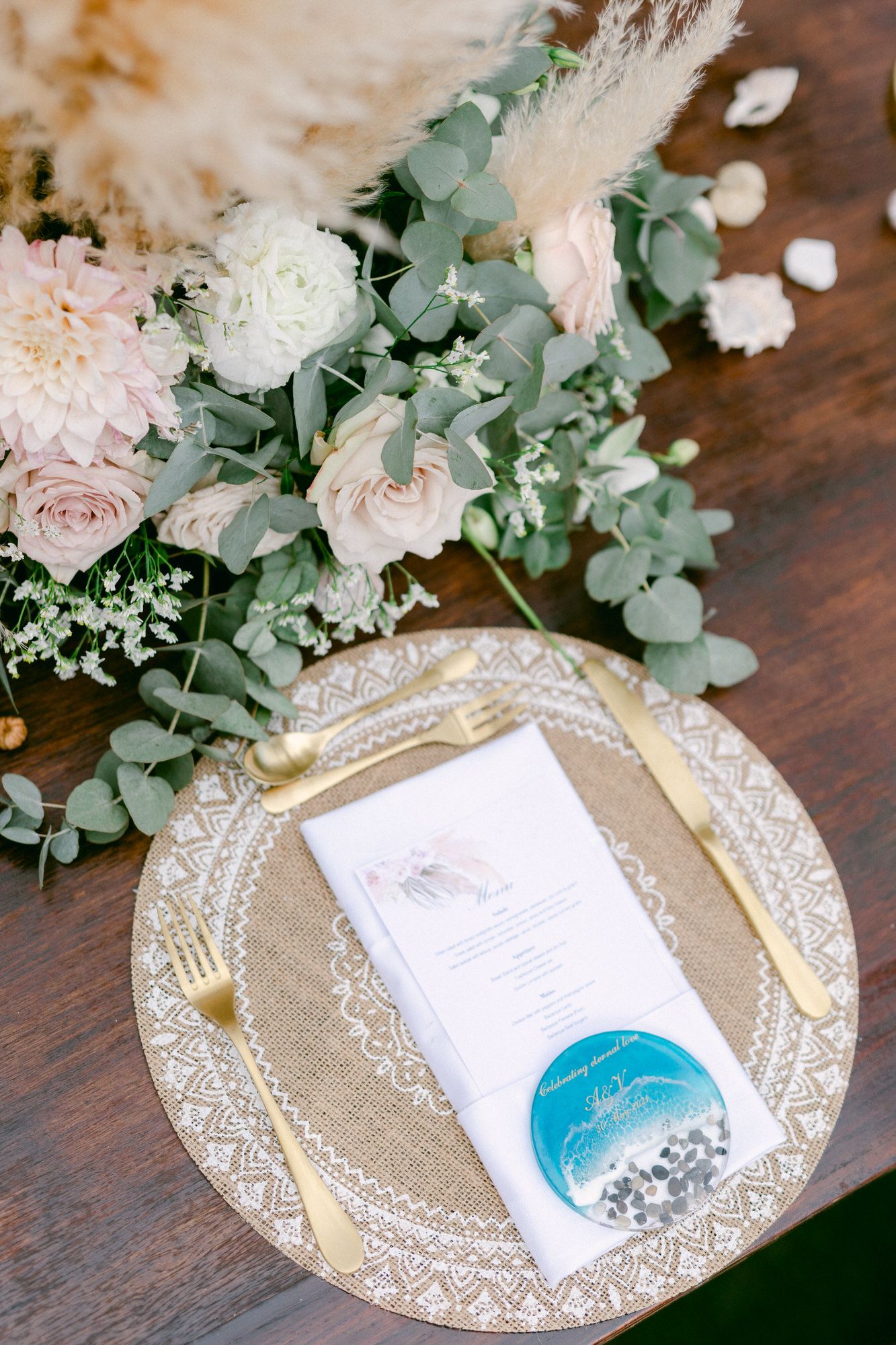 Elegant place setting with pink florals, eucalyptus and wedding menu on gold charger plate.