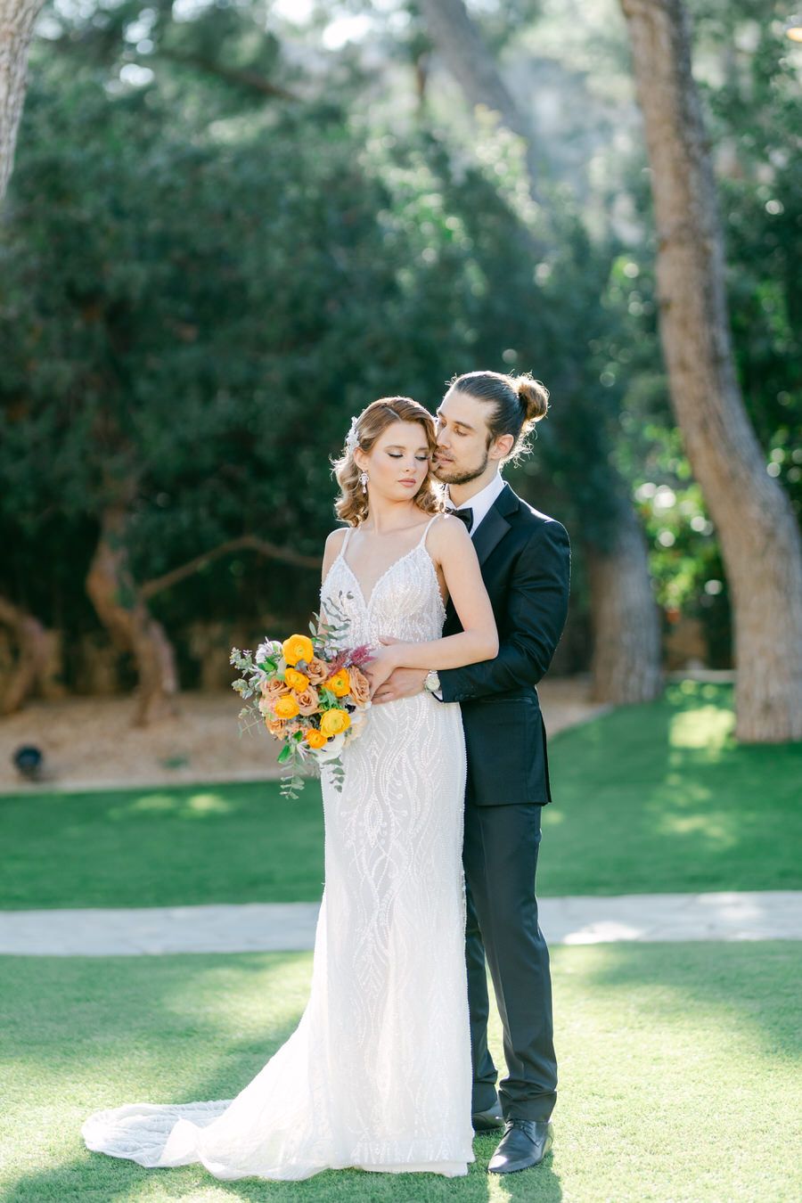 Romantic wedding portrait with bride holding orange bouquet against garden backdrop.