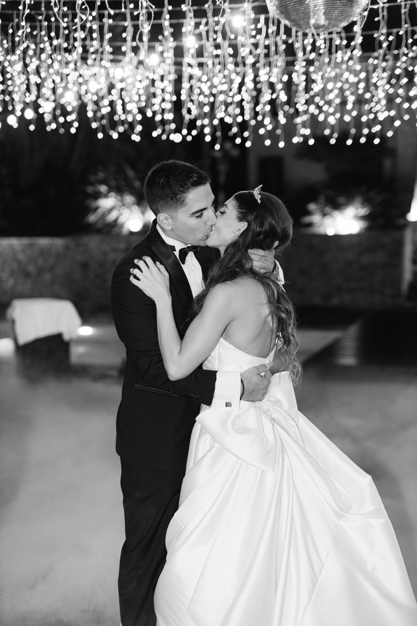 A couple shares their first dance as newlyweds under sparkling crystal chandeliers in an elegant ballroom setting.