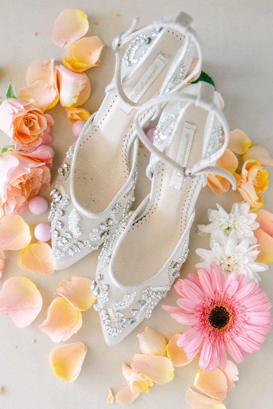 Elegant bridal shoes with crystal details surrounded by pink petals and gerbera daisies.