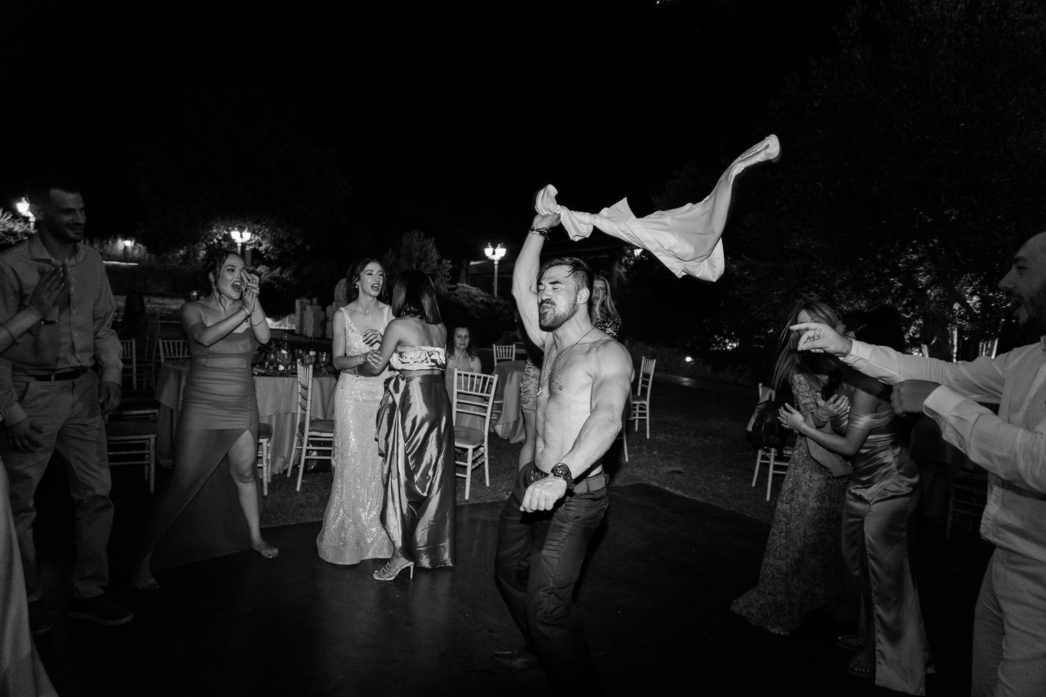 A black and white wedding reception photo showing a lively dance floor with guests celebrating and waving napkins in the air.
