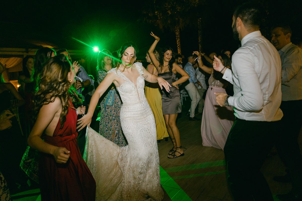 Wedding celebration on a dance floor illuminated by green lights as guests dance together.