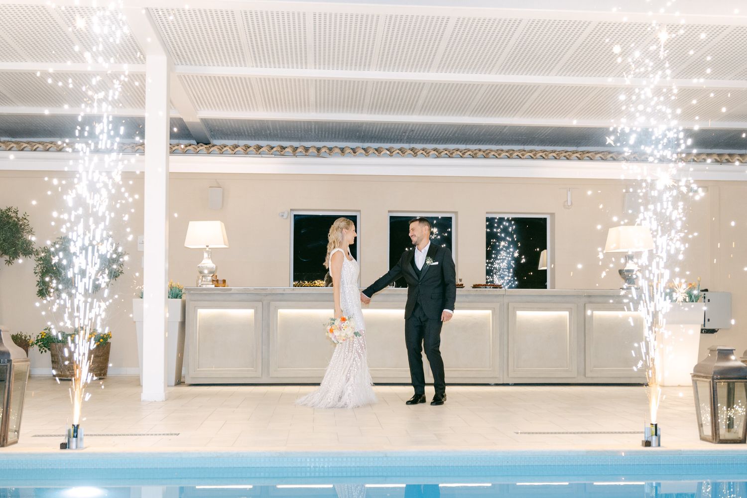 Elegant wedding celebration at indoor venue with sparkler fountains and pool creating magical atmosphere during evening reception.