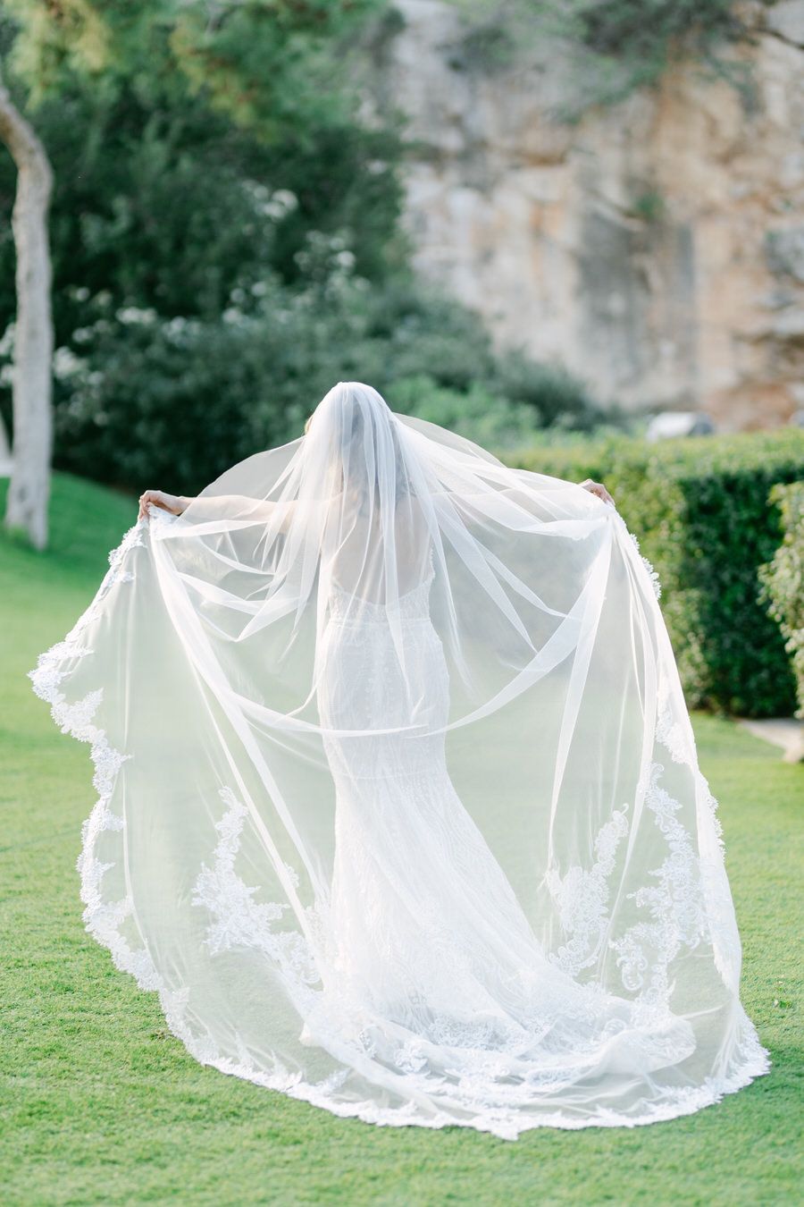 Ethereal bridal portrait with flowing lace veil against natural outdoor backdrop.