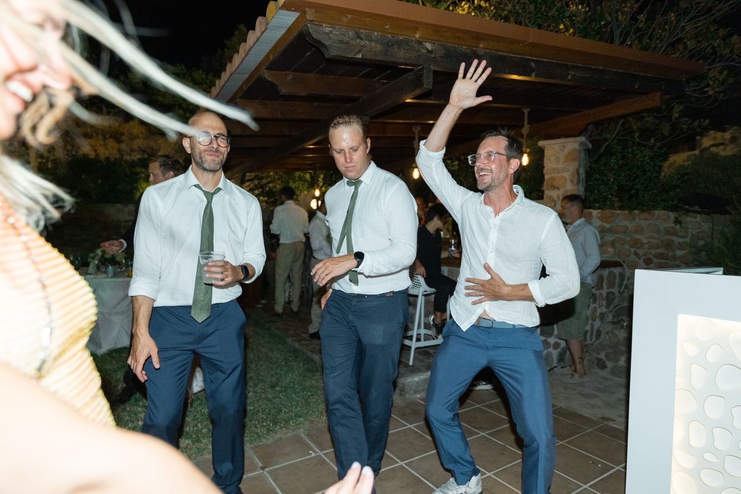 Three guests dancing energetically at an outdoor evening party.