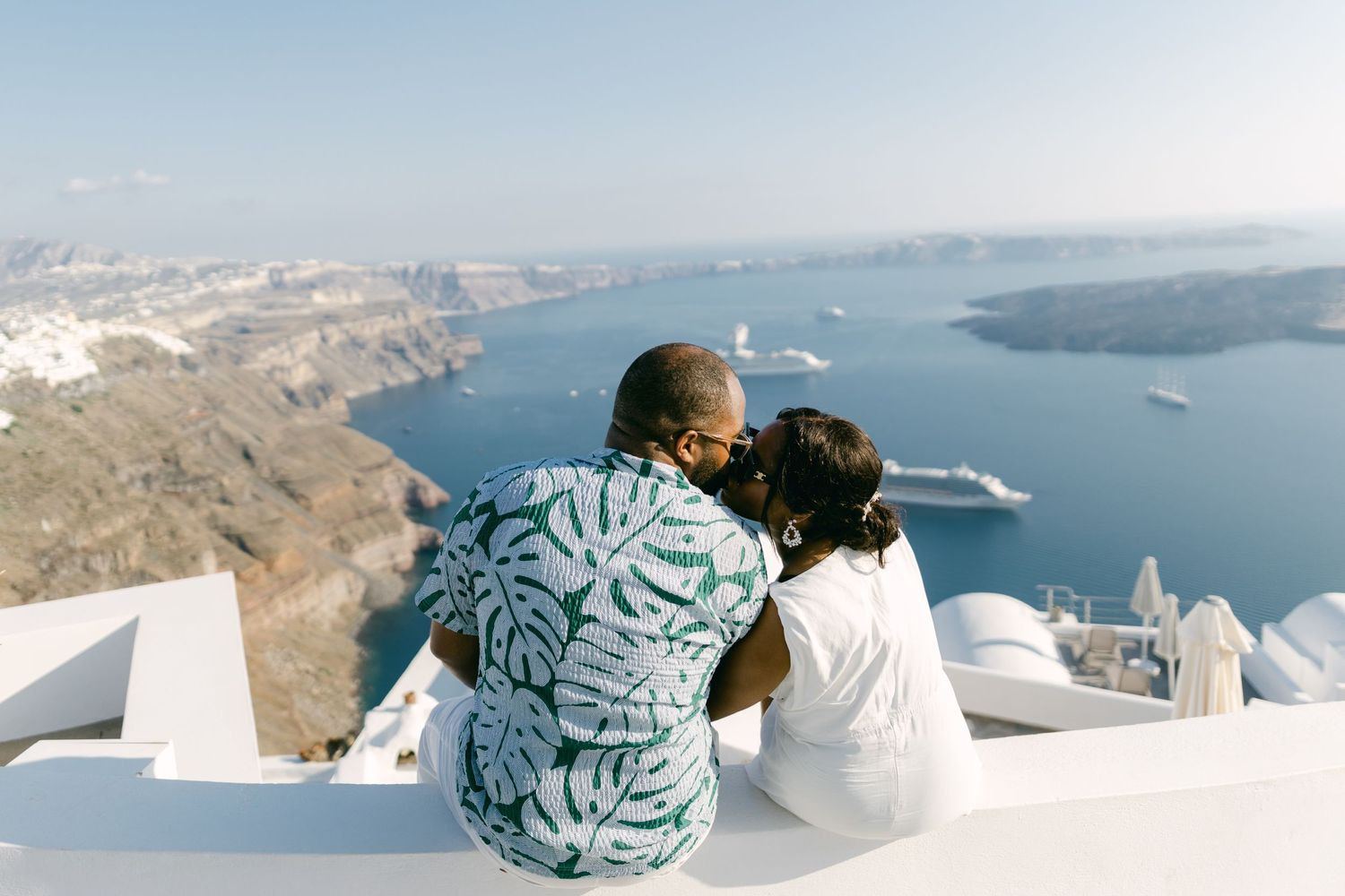 Two people sitting on white steps overlooking the stunning caldera views of Santorini.