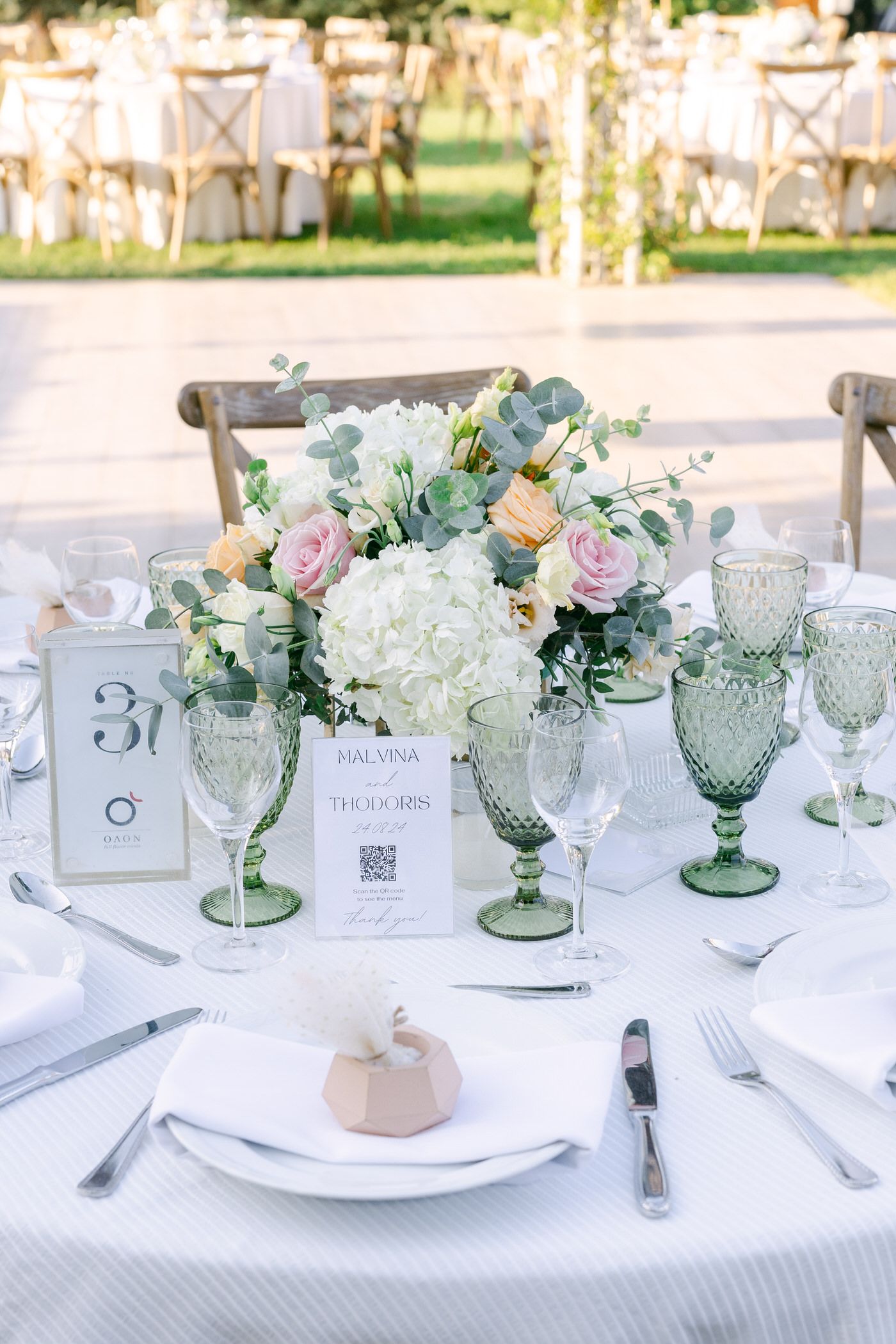 Elegant wedding table setting with pastel floral centerpiece, vintage green glassware, and white table linens.