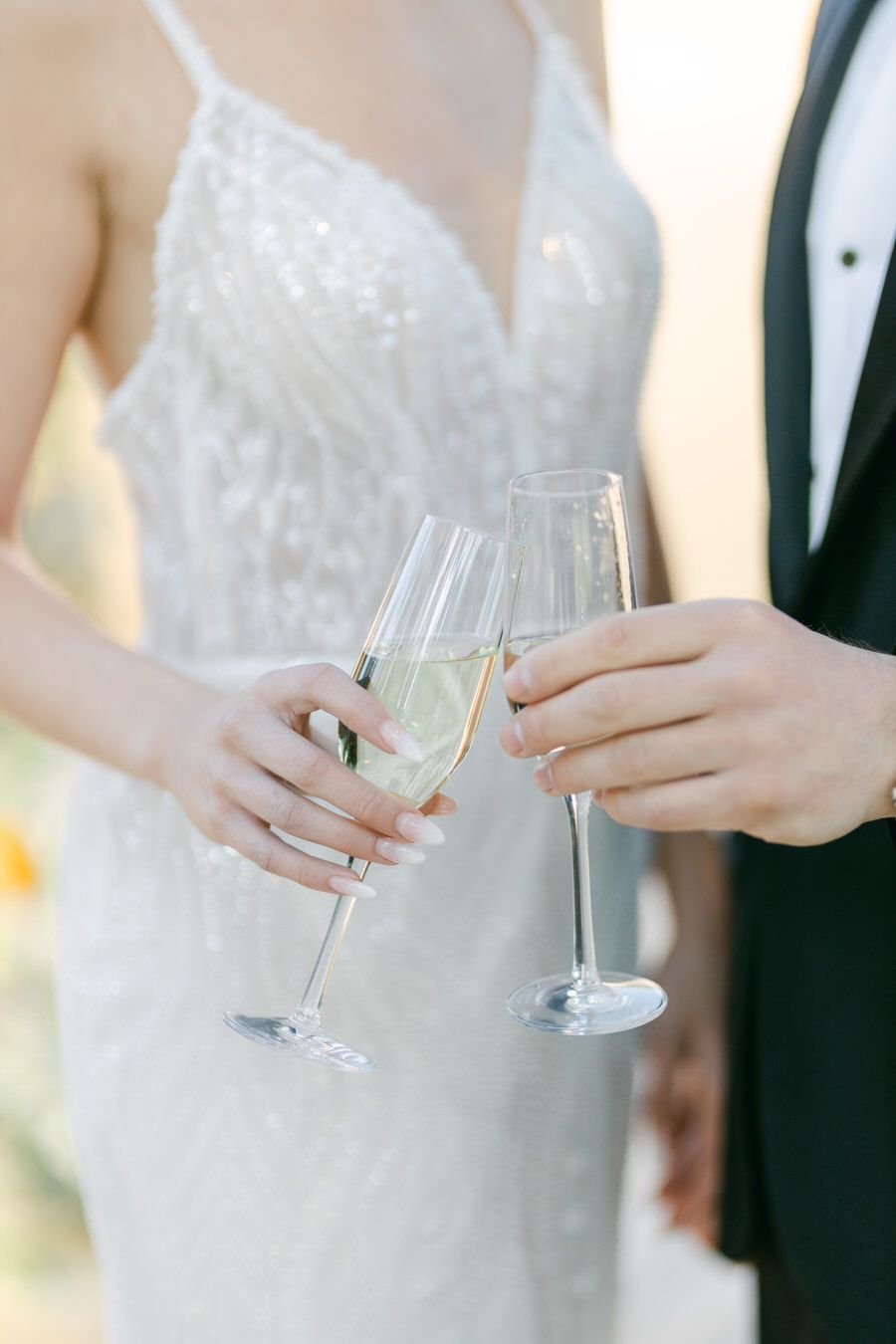 Close-up of champagne toast with elegant wedding dress and tuxedo details.