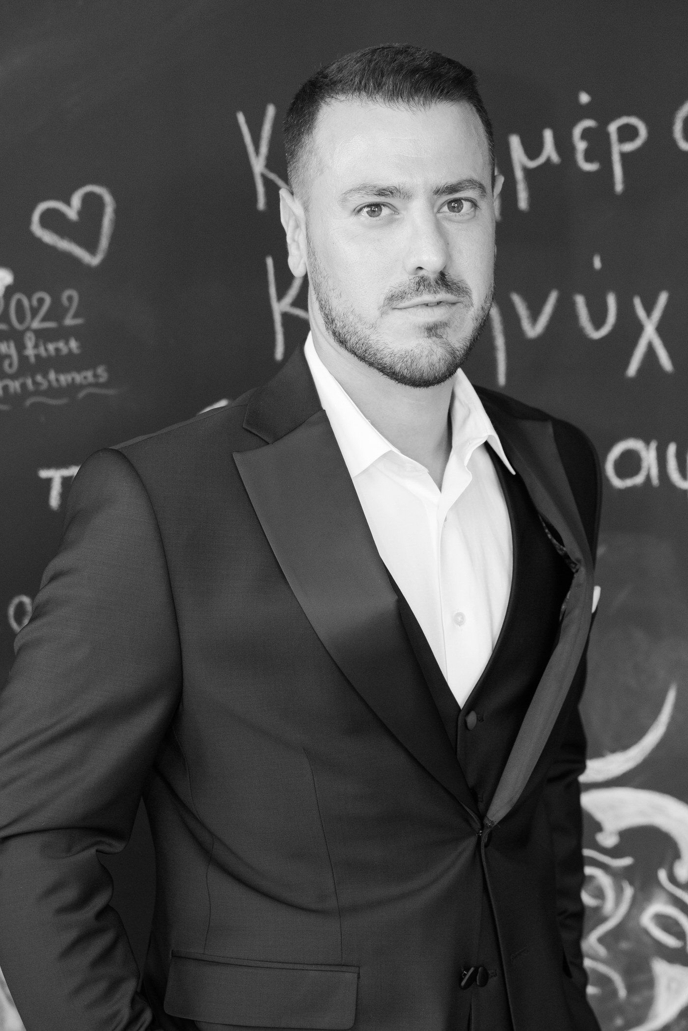 Black and white portrait of a person in a suit standing in front of a chalkboard with writing and symbols.