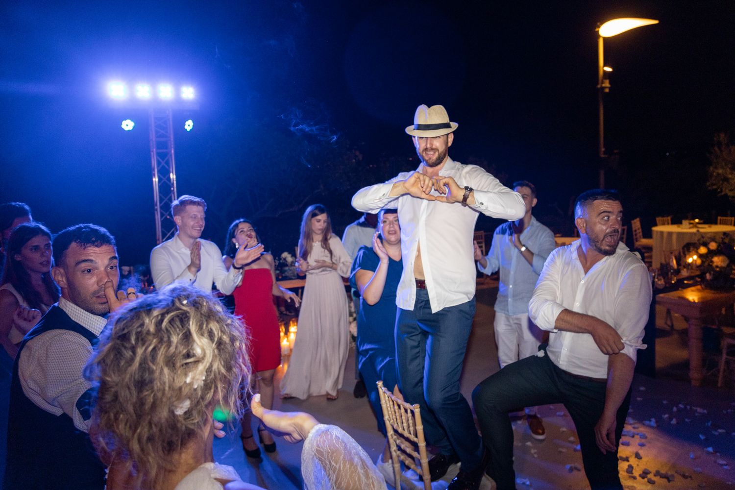 A lively dance party scene at an outdoor nighttime event with bright blue spotlights illuminating the crowd.