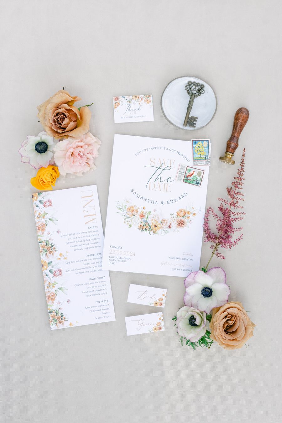 Wedding invitation set with antique key, vintage stamps, and fresh flower accents on light background.