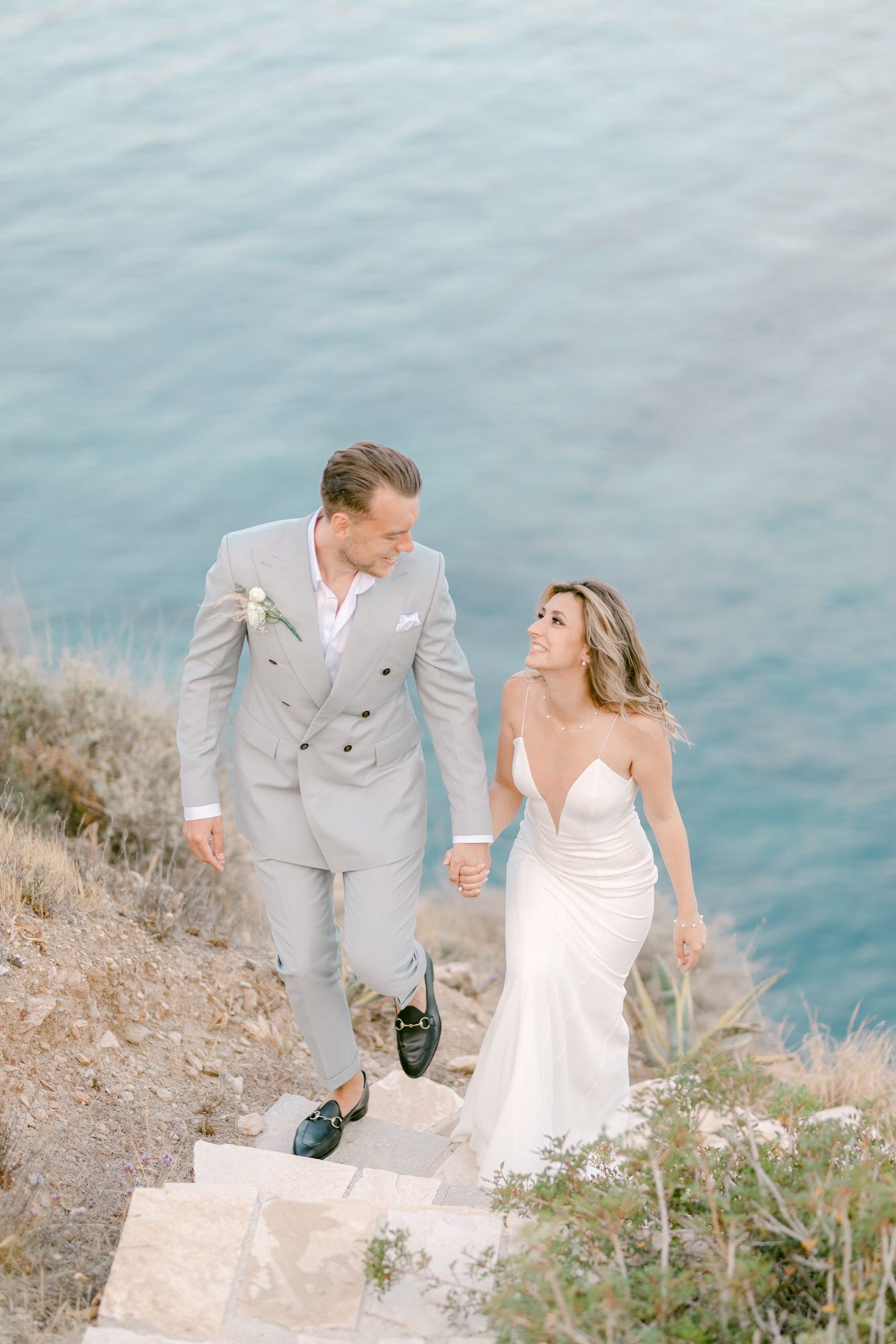 A couple walking up stone steps overlooking Mediterranean blue waters.