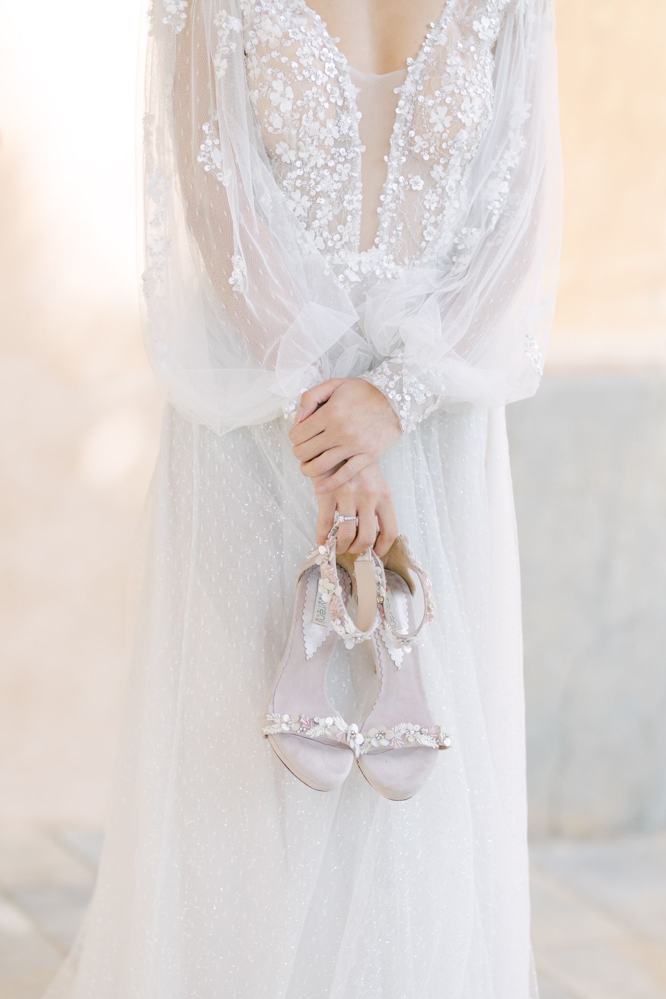 Close-up detail of a delicate white lace wedding dress with billowing sleeves holding embellished bridal shoes.