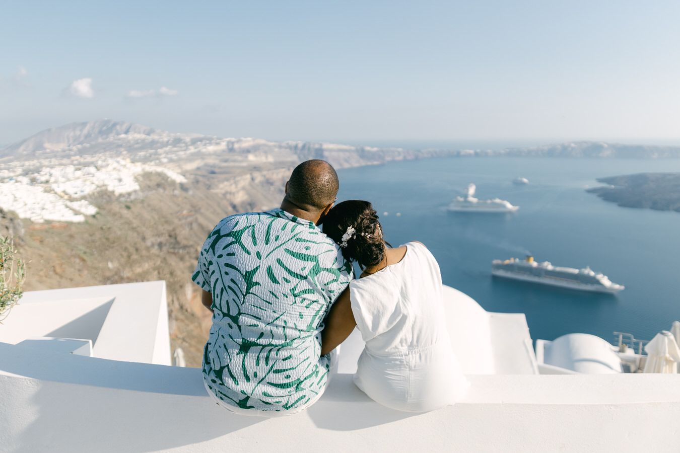 Five scenic photos of white buildings overlooking the blue waters of Santorini Greece with distant cruise ships.