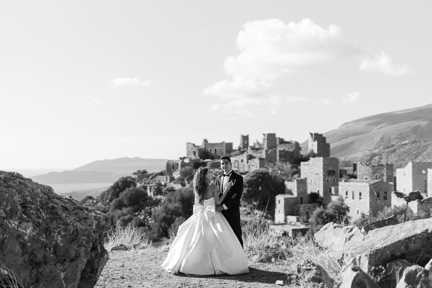 A scenic black and white view of a bride in wedding dress overlooking a medieval hilltop castle town.
