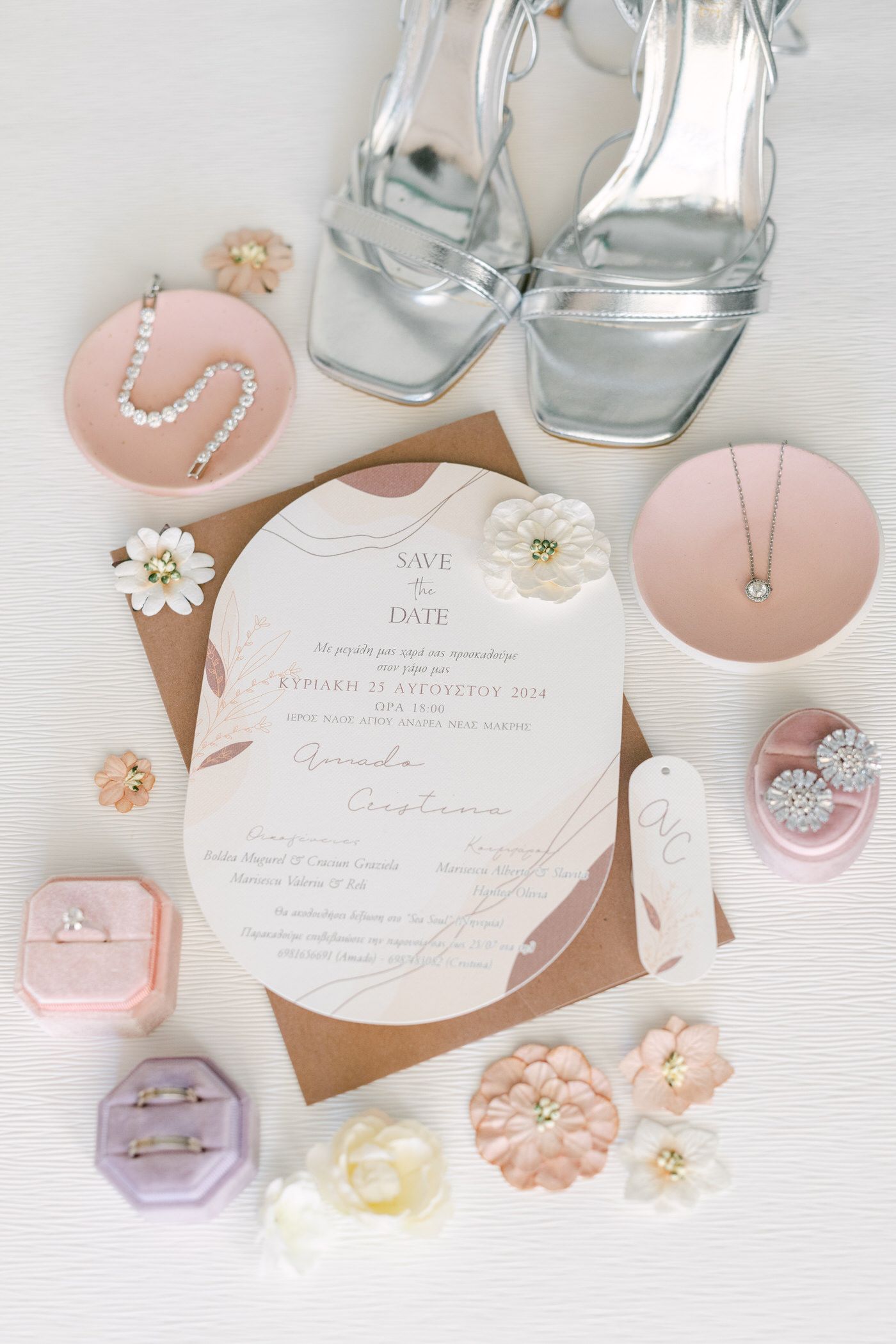 Wedding invitation flatlay with silver heels, pink and white accessories, and delicate floral details on white background.