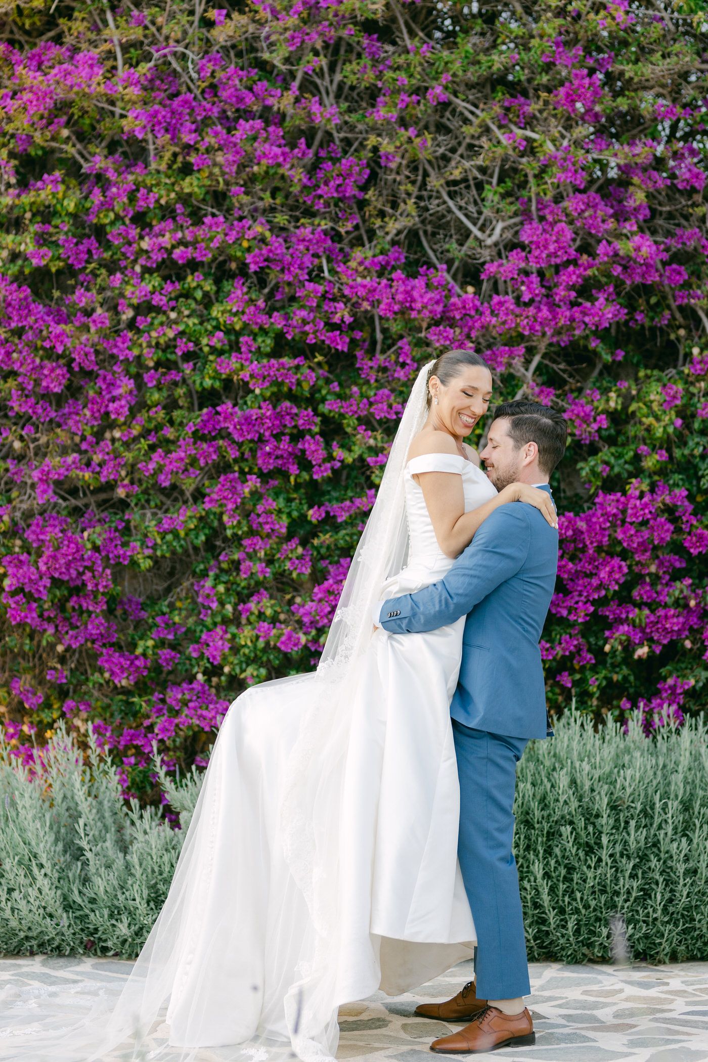 A romantic moment in front of a vibrant purple bougainvillea wall with sage plants in the foreground.