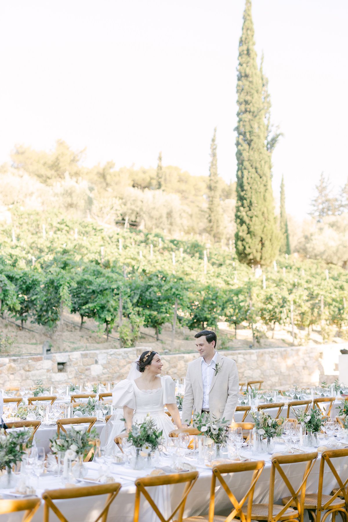 Elegant outdoor wedding reception table setup in a Tuscan garden with wooden chairs and cypress trees in the background.