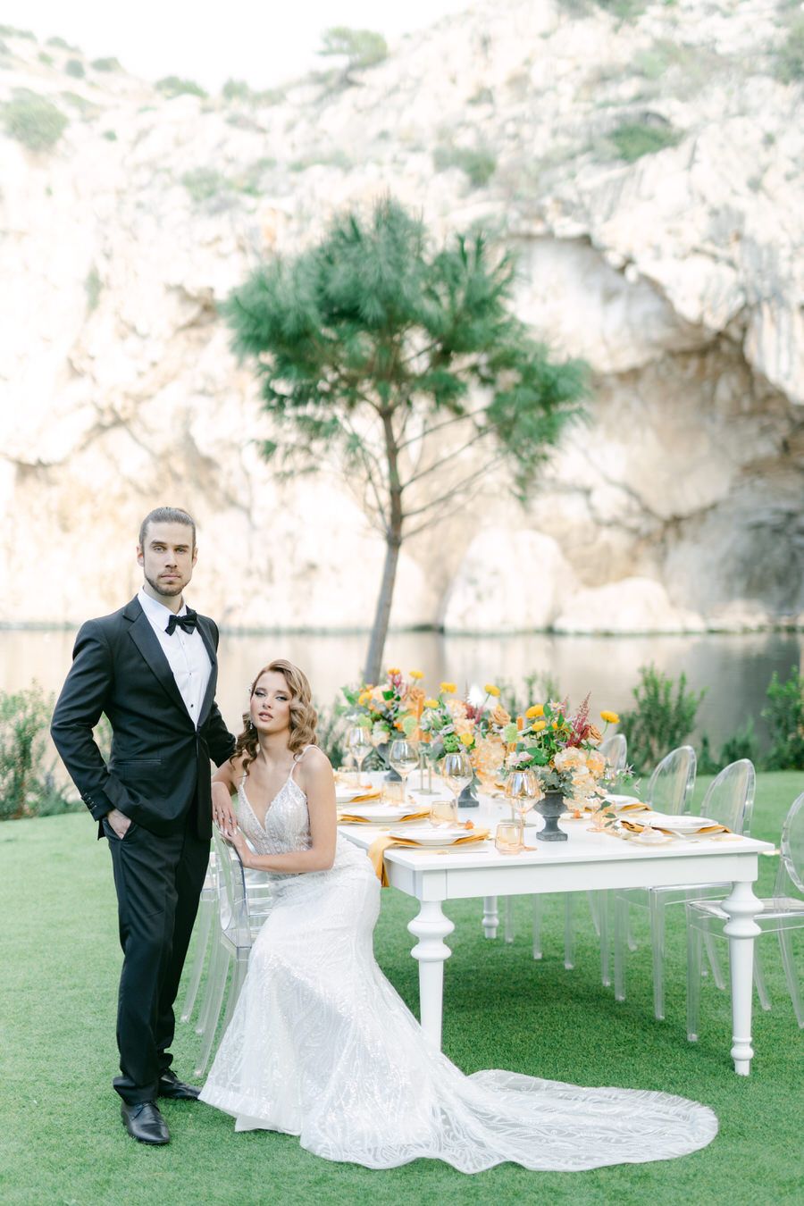 An elegant wedding table setup against limestone cliffs with a couple posing nearby.