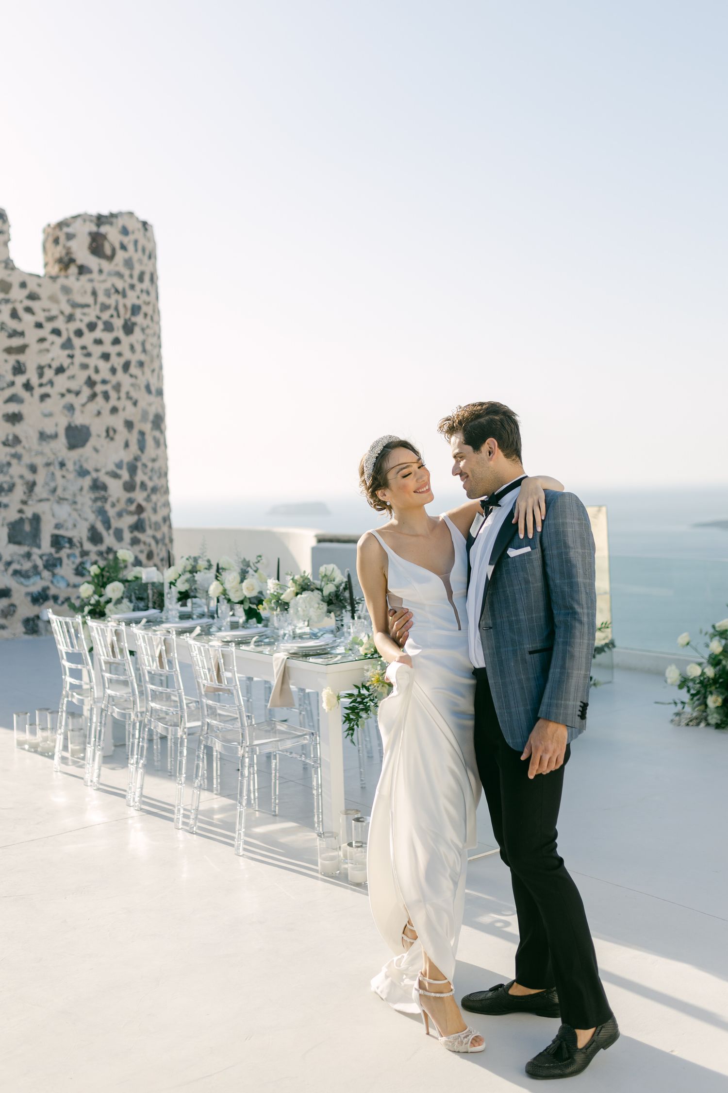 Wedding couple on white terrace with ocean view and clear ghost chairs setup.