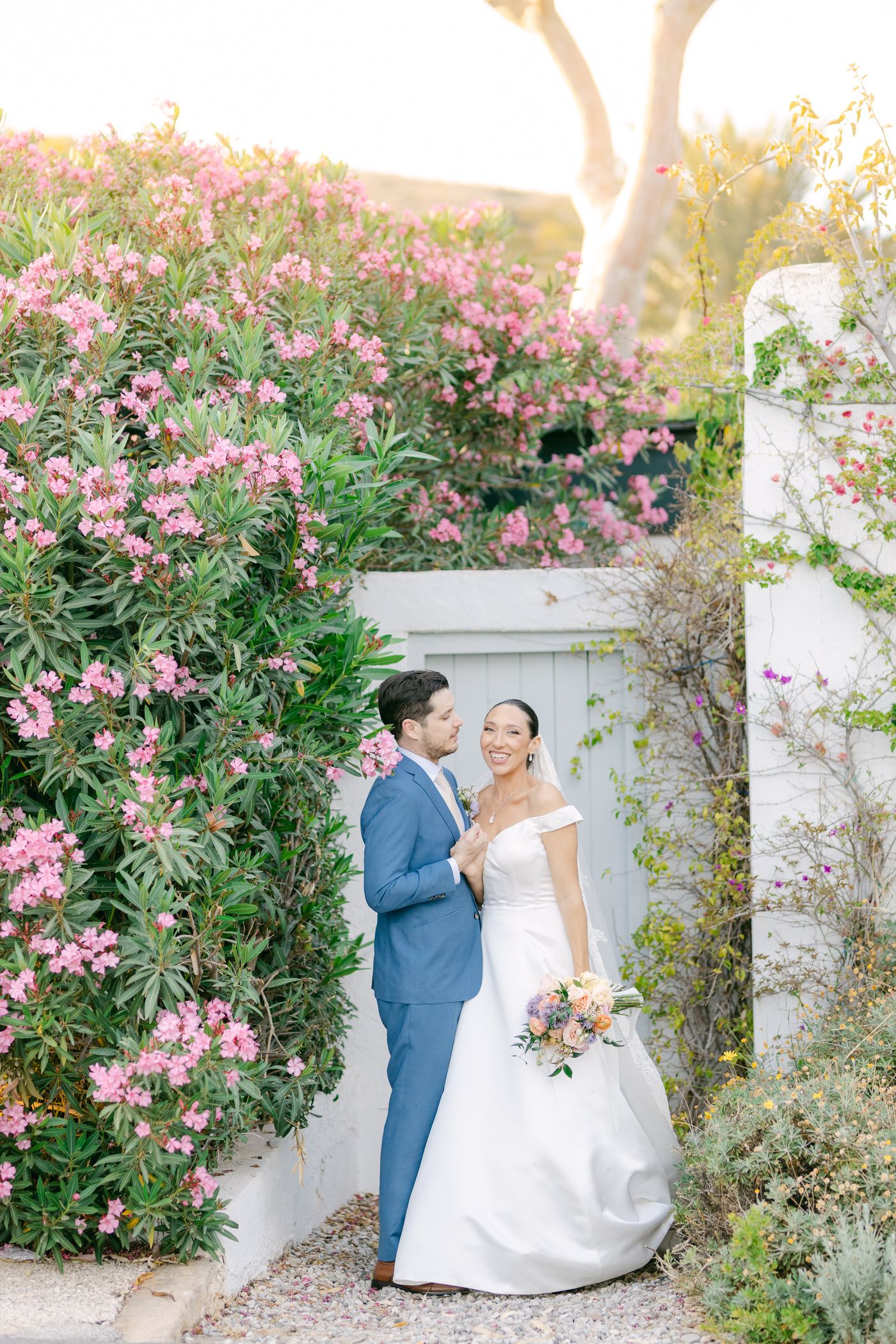 A romantic garden wedding scene with pink oleander flowers blooming against a white wall during golden hour.