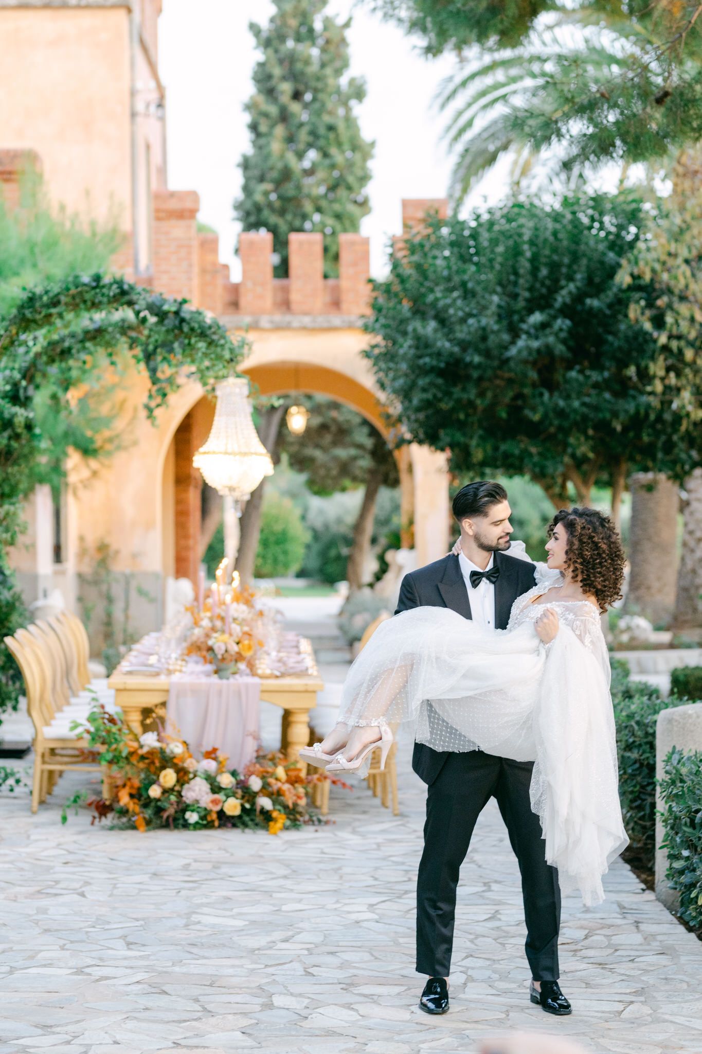 Romantic wedding couple share an intimate moment in a Mediterranean courtyard with elegant table decor and floral arrangements.