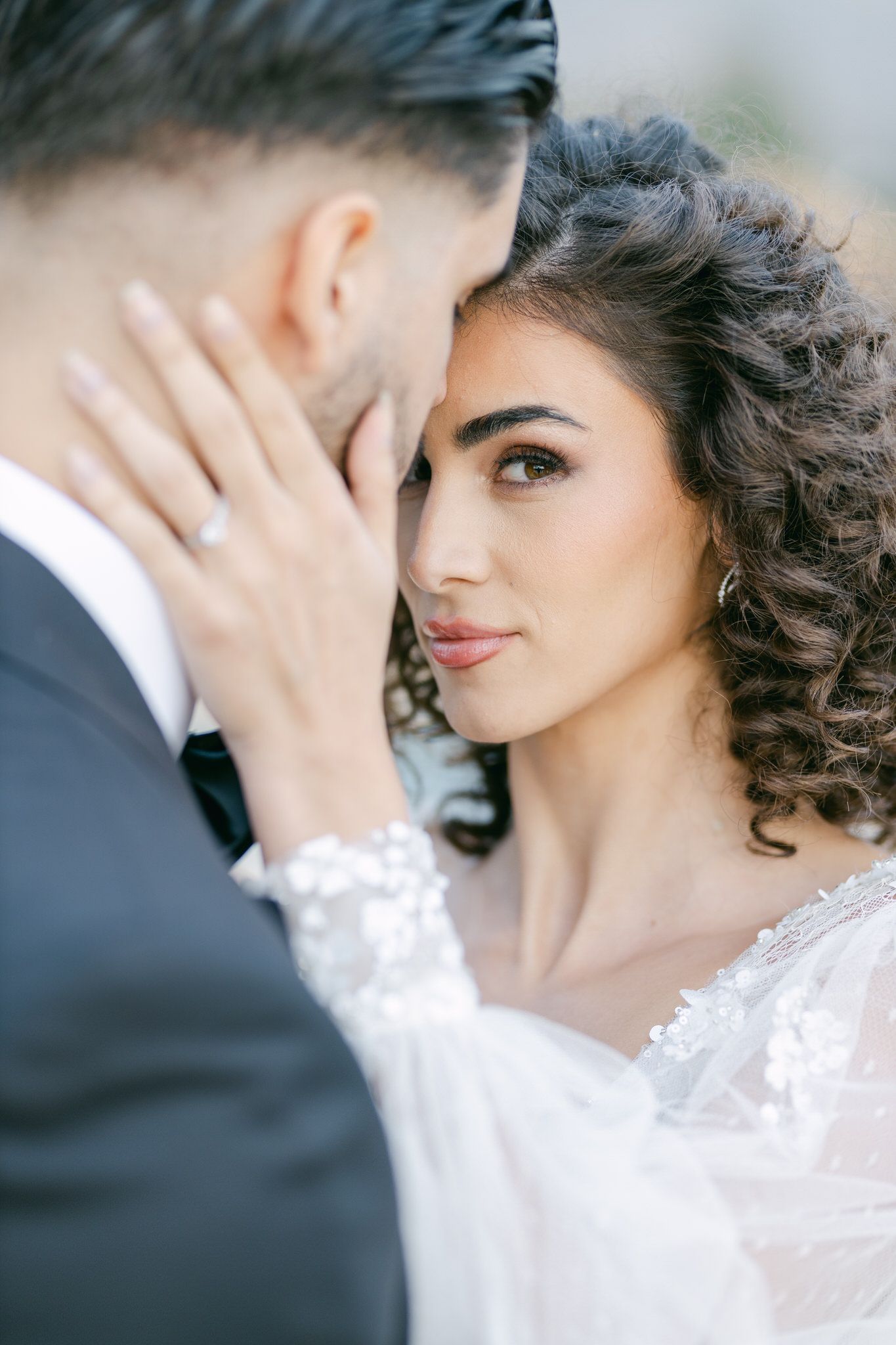 A romantic wedding portrait showing a tender moment between a bride in a lace dress and groom in a dark suit.