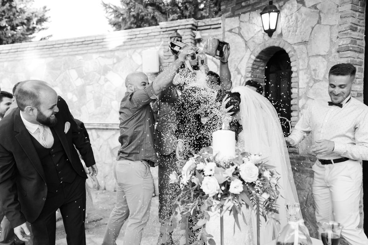 Black and white photo of a joyful wedding celebration with confetti being tossed at a stone archway entrance.