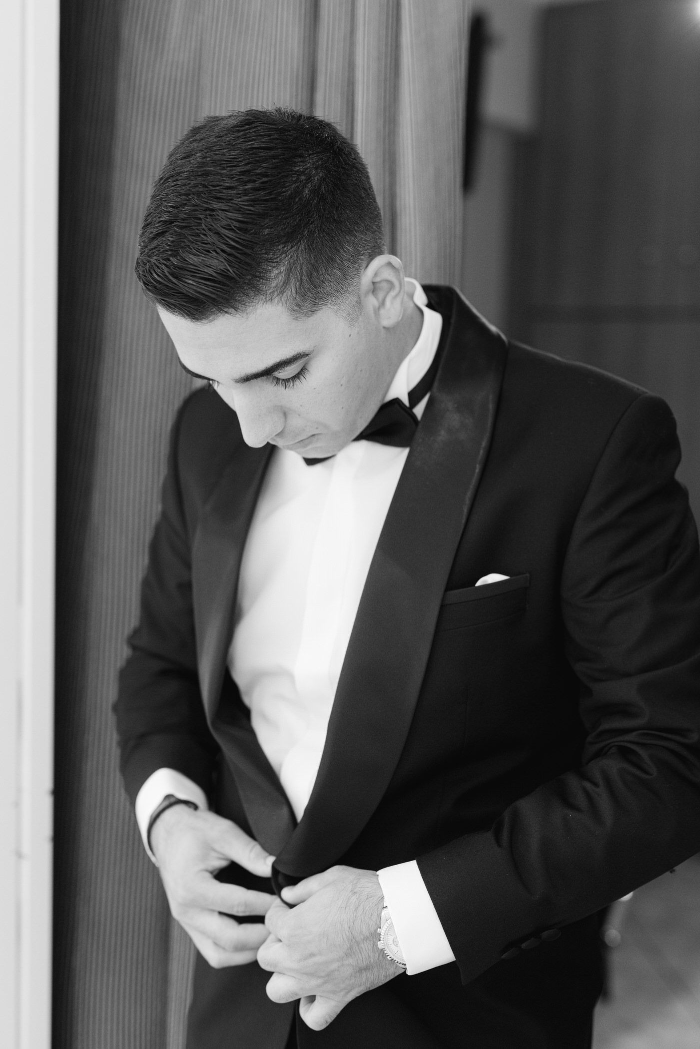 Black and white photo of person in formal tuxedo adjusting their button while getting ready.