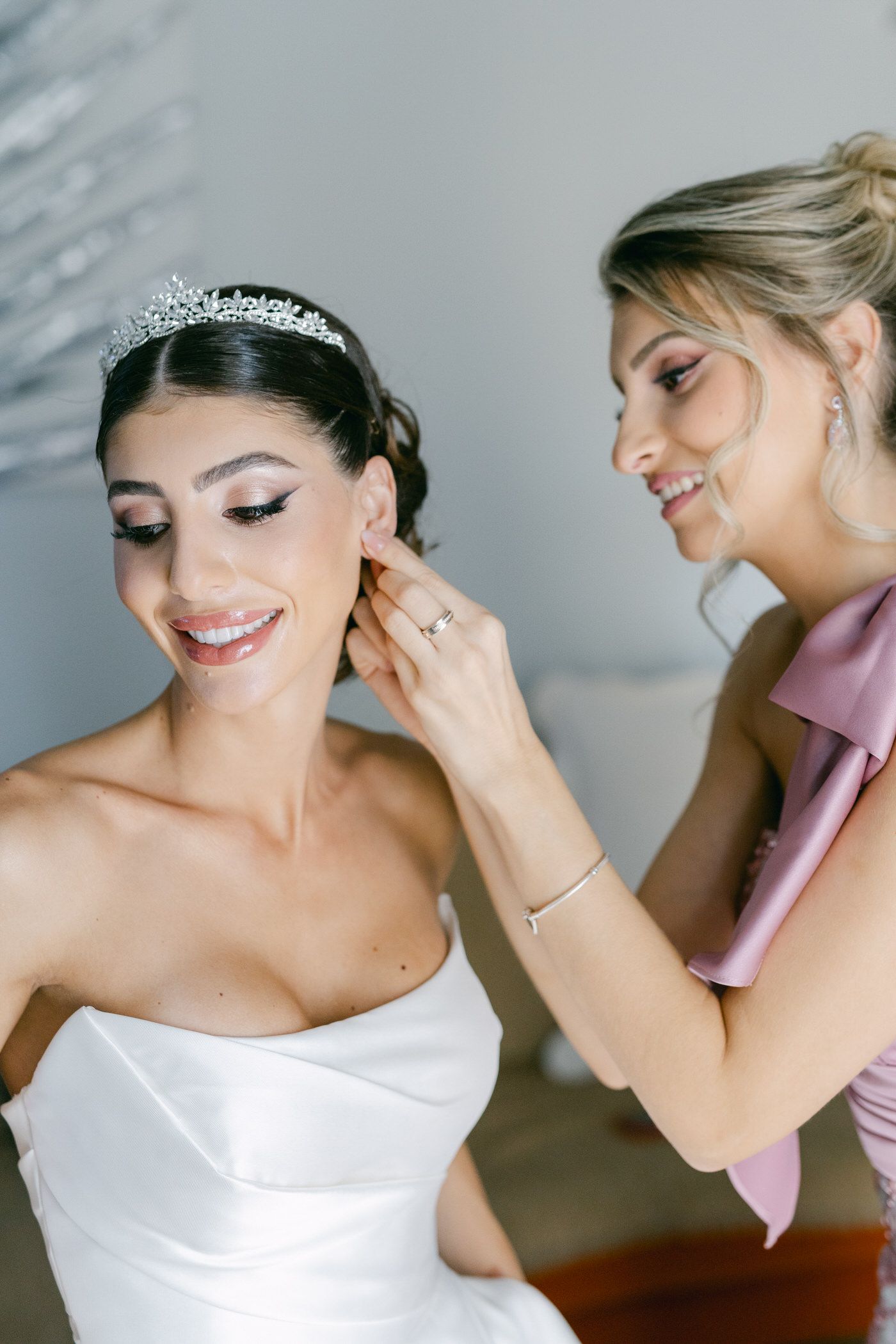 Beautiful wedding preparation scene shows bride in strapless gown getting help with final touches.