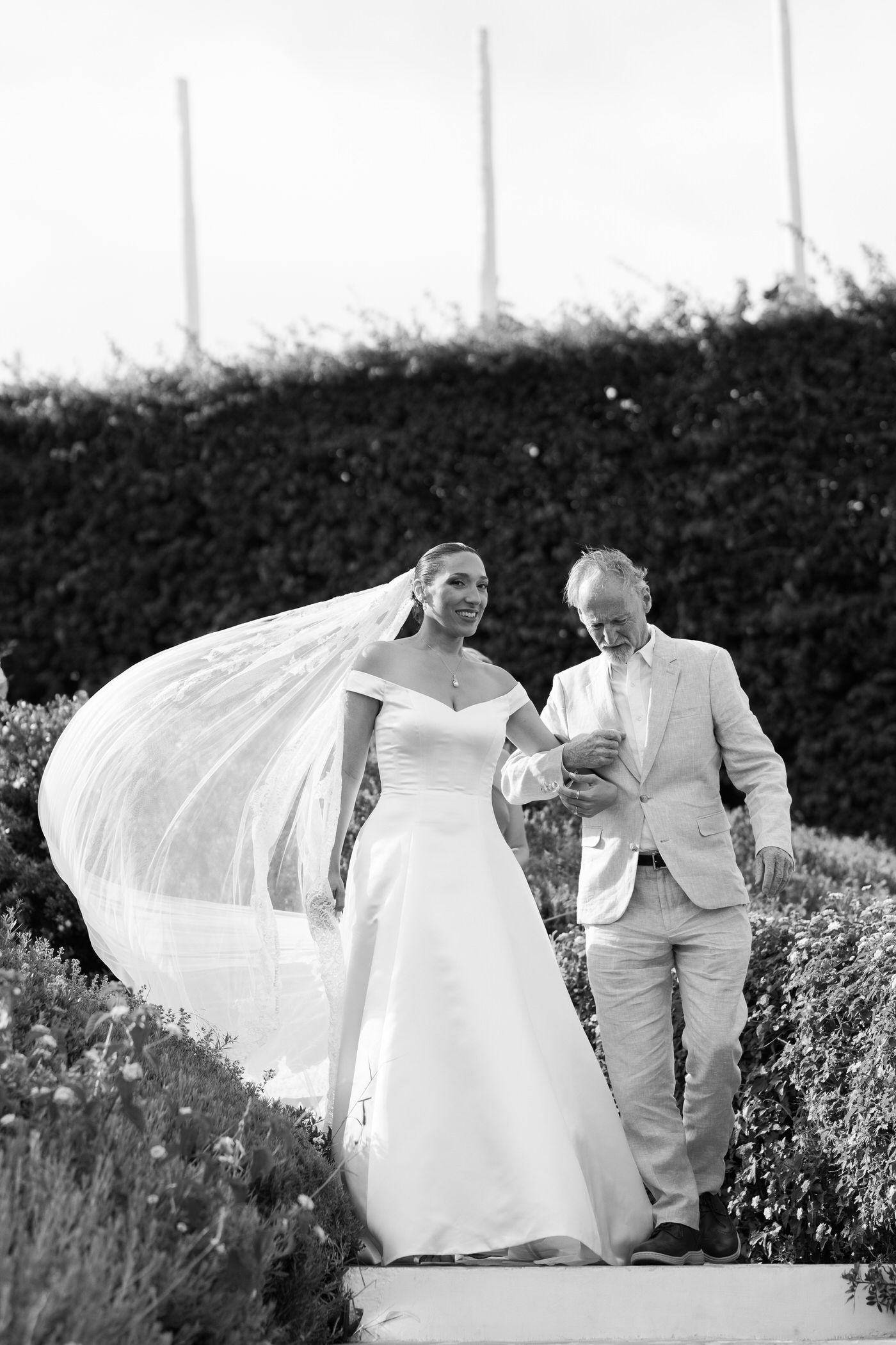 A beautiful black and white wedding photo captures a couple walking together with the bride's veil flowing in the wind.