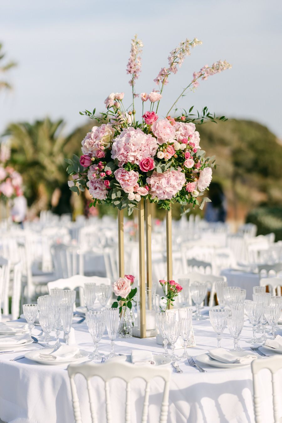 Elegant pink and white floral centerpiece on gold stands at wedding reception table.