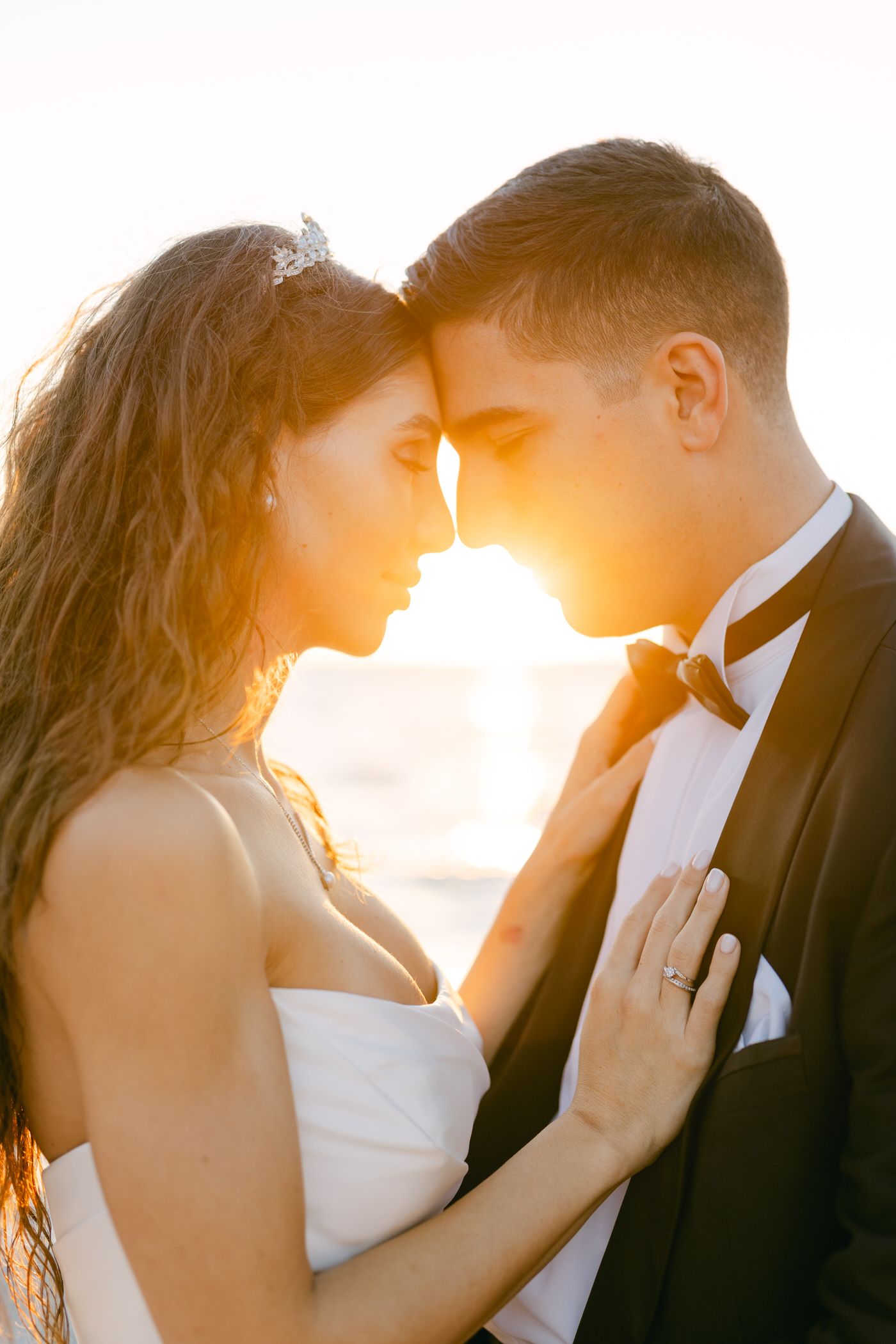 A backlit wedding couple sharing an intimate moment at sunset with warm golden lighting.