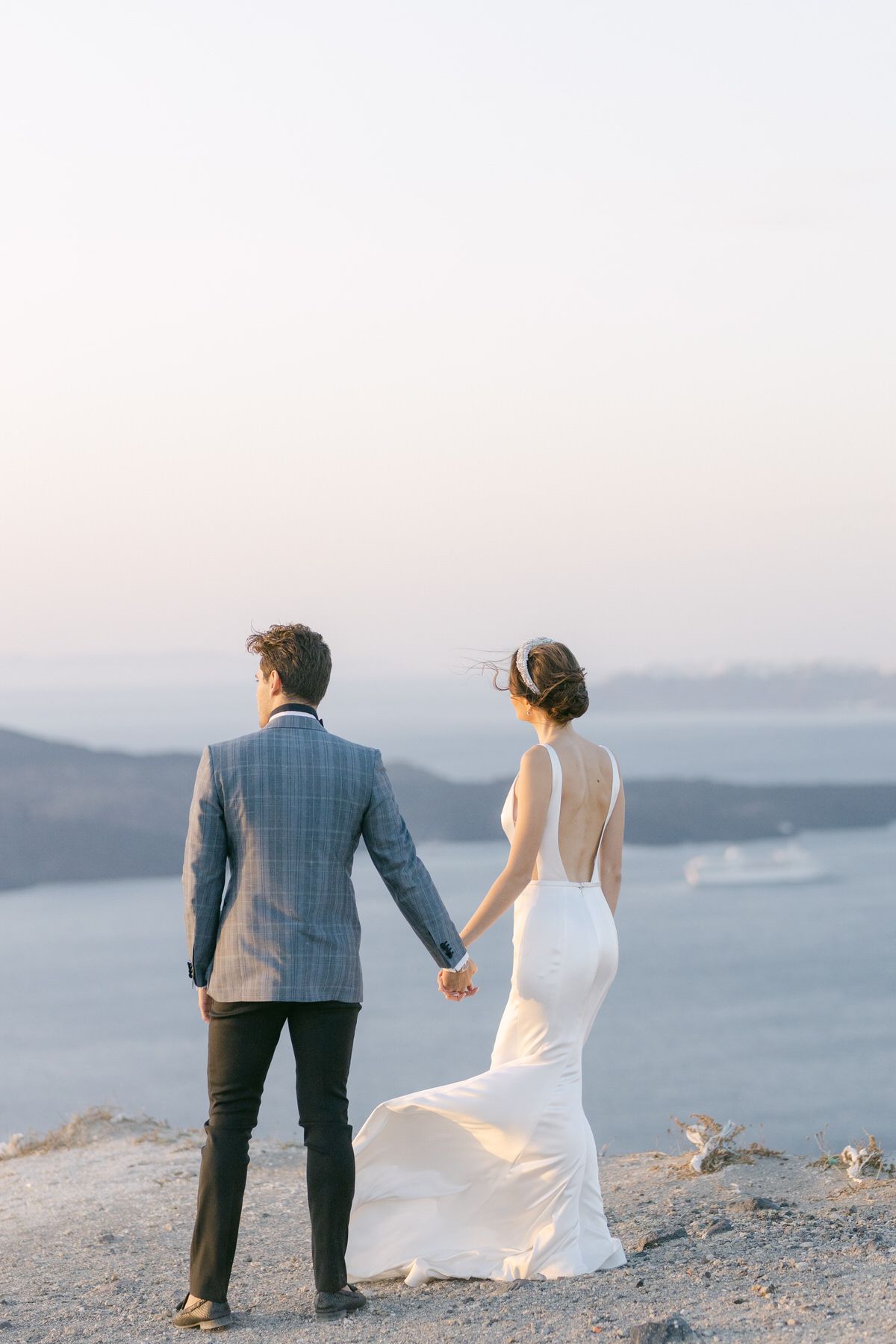 A couple in wedding attire holding hands while overlooking a misty mountain landscape at sunset.