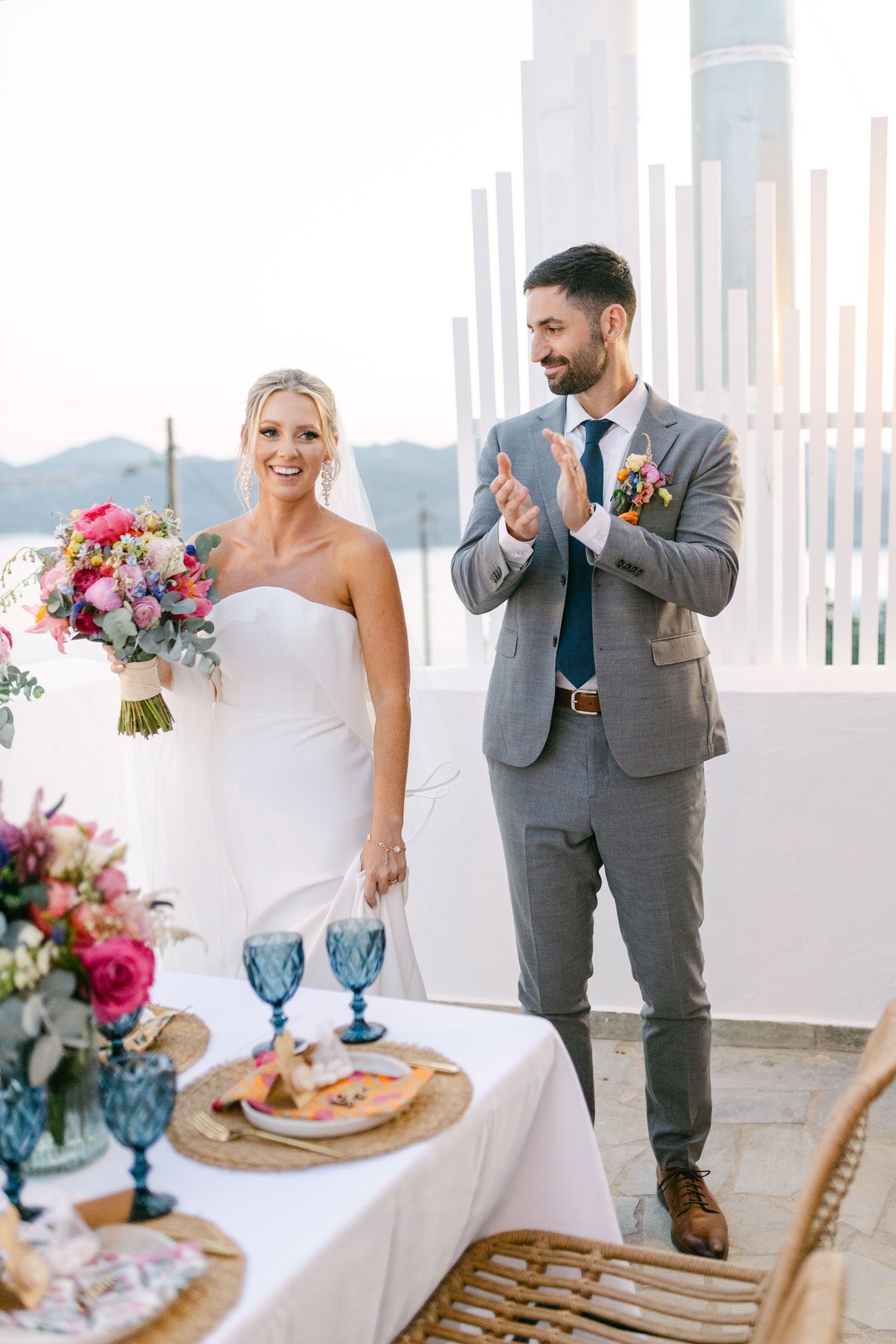 Elegant wedding reception setup with blue glassware and floral arrangements on white tablecloth against scenic mountain backdrop.