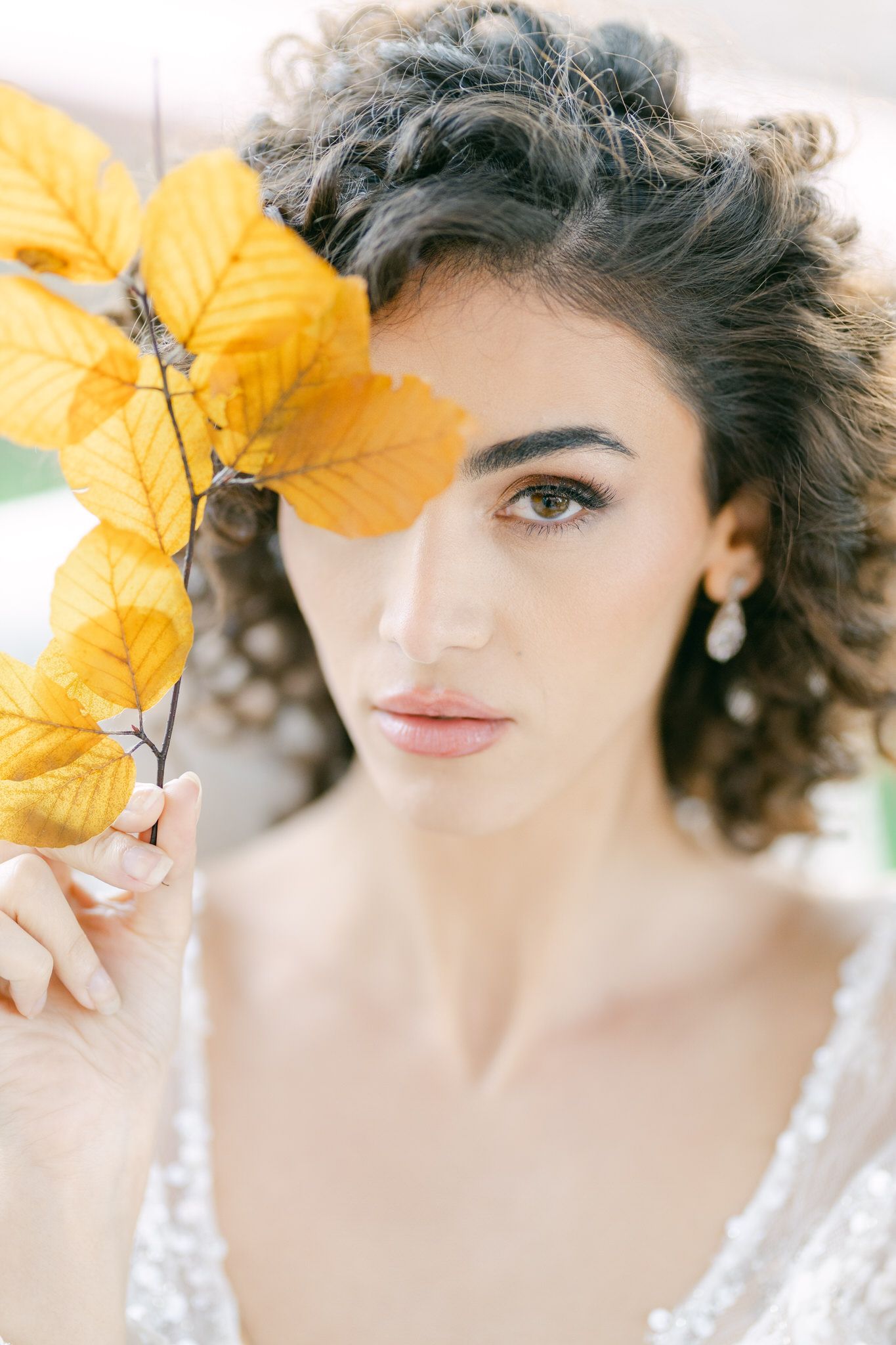 A soft ethereal autumn portrait features golden leaves and pearl earrings against a light dreamy background.