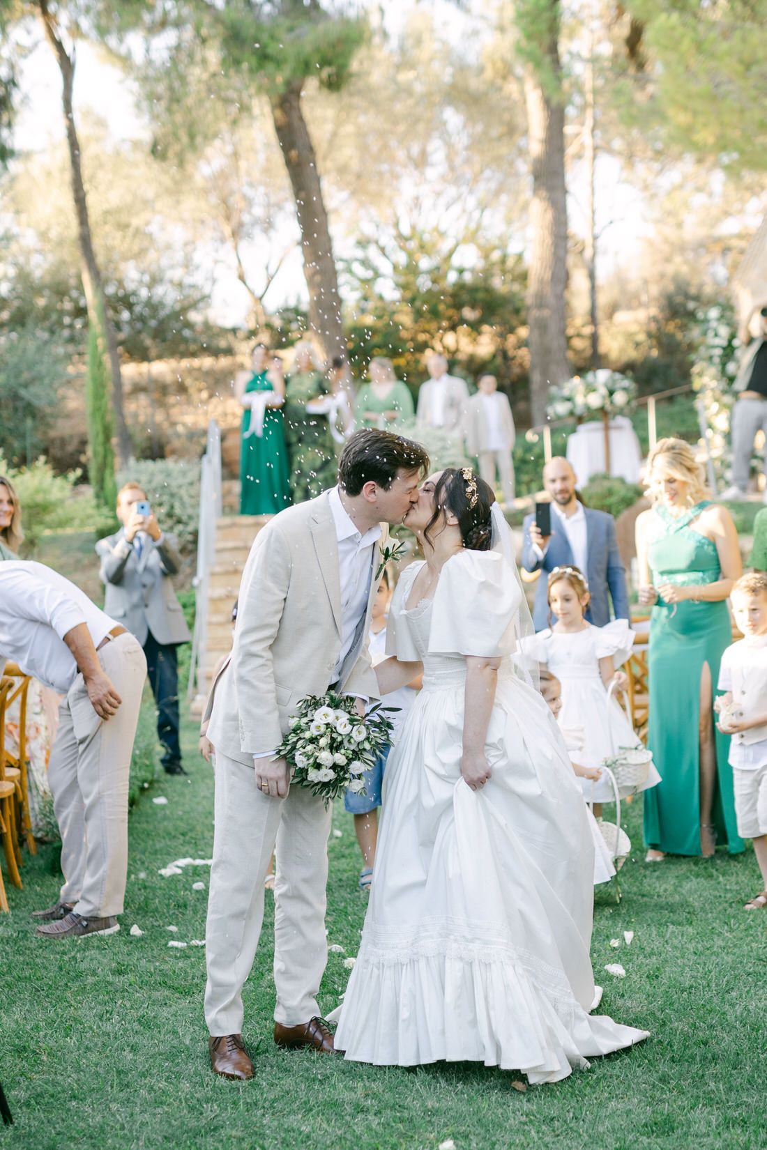 A romantic outdoor garden wedding ceremony with bridesmaids in green dresses and the couple sharing a tender moment.