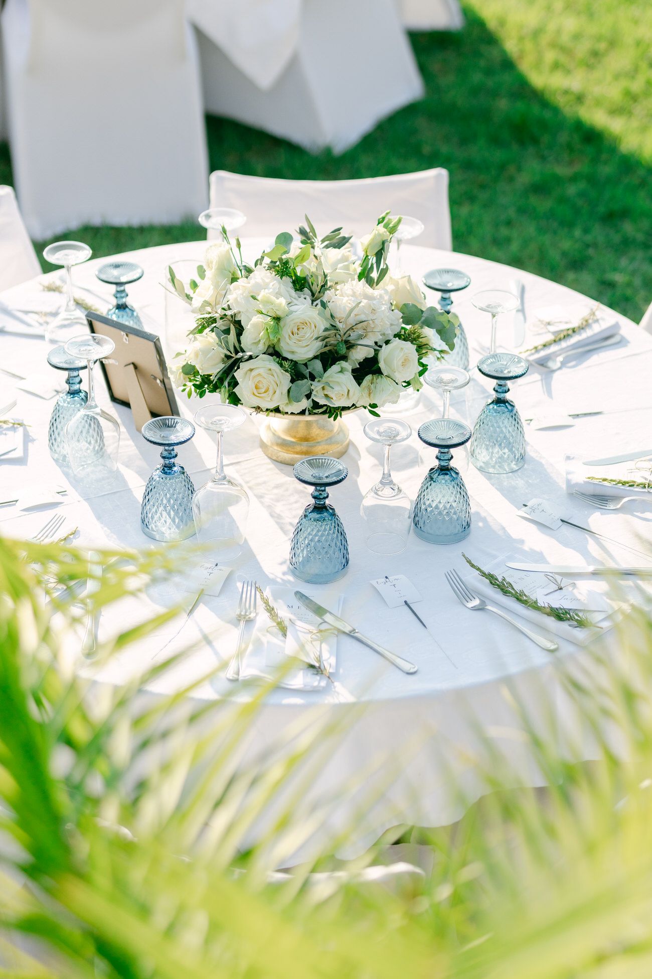 Elegant wedding table setting with blue glasses and white floral centerpiece.