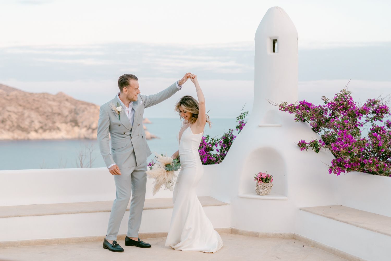A wedding couple dancing on a white terrace with traditional Greek architecture and sea views.
