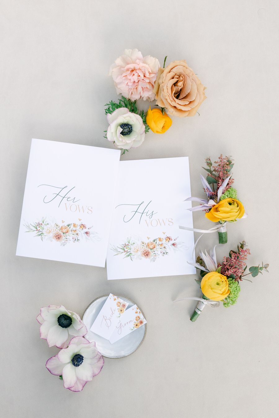 Flat lay of wedding stationery with delicate floral details and pastel boutonnieres.